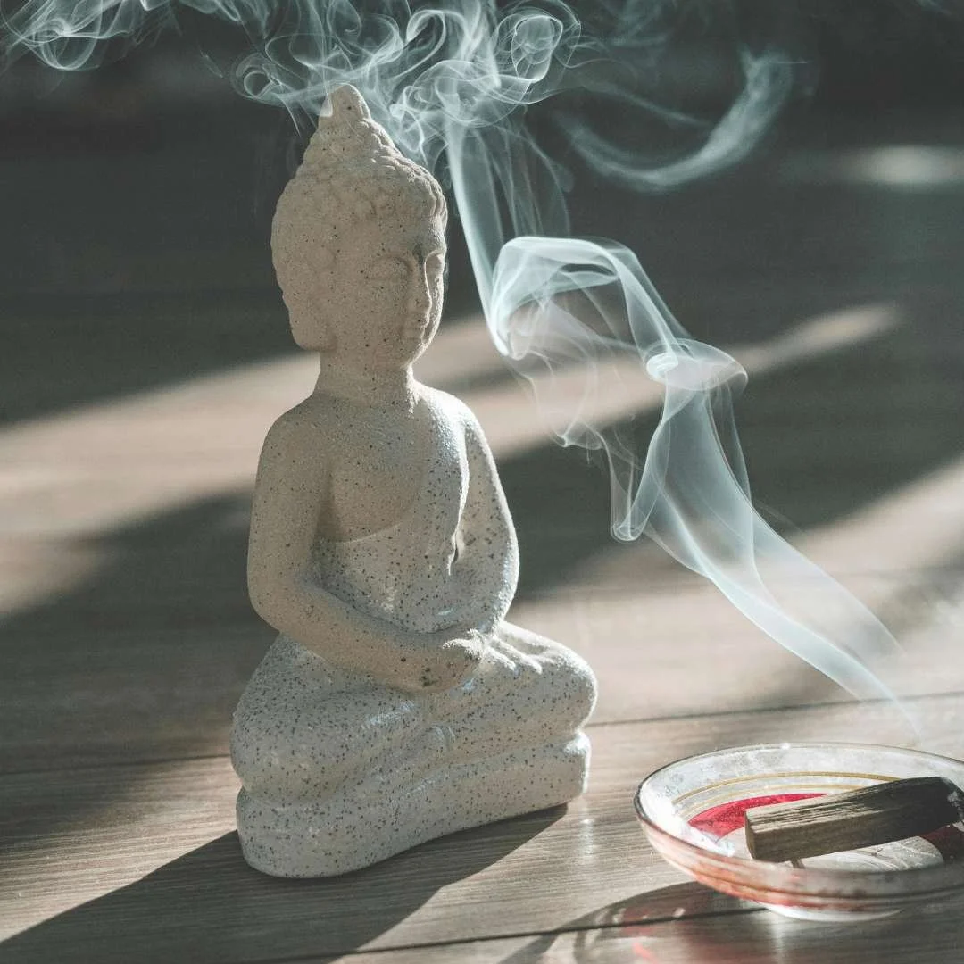 Buddha statue with rising incense smoke in soft natural light, reflecting the calm and grounding atmosphere of Private Yoga sessions with Mel Rolfes.