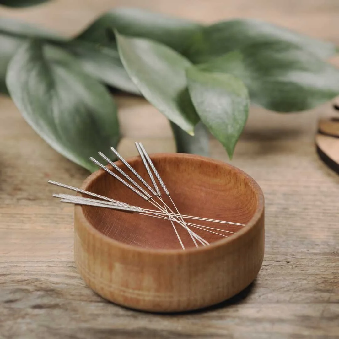 Acupuncture needles resting in a wooden bowl, representing ear acupuncture and 5 Needle Protocol sessions offered by Mel Rolfes in Roanoke.