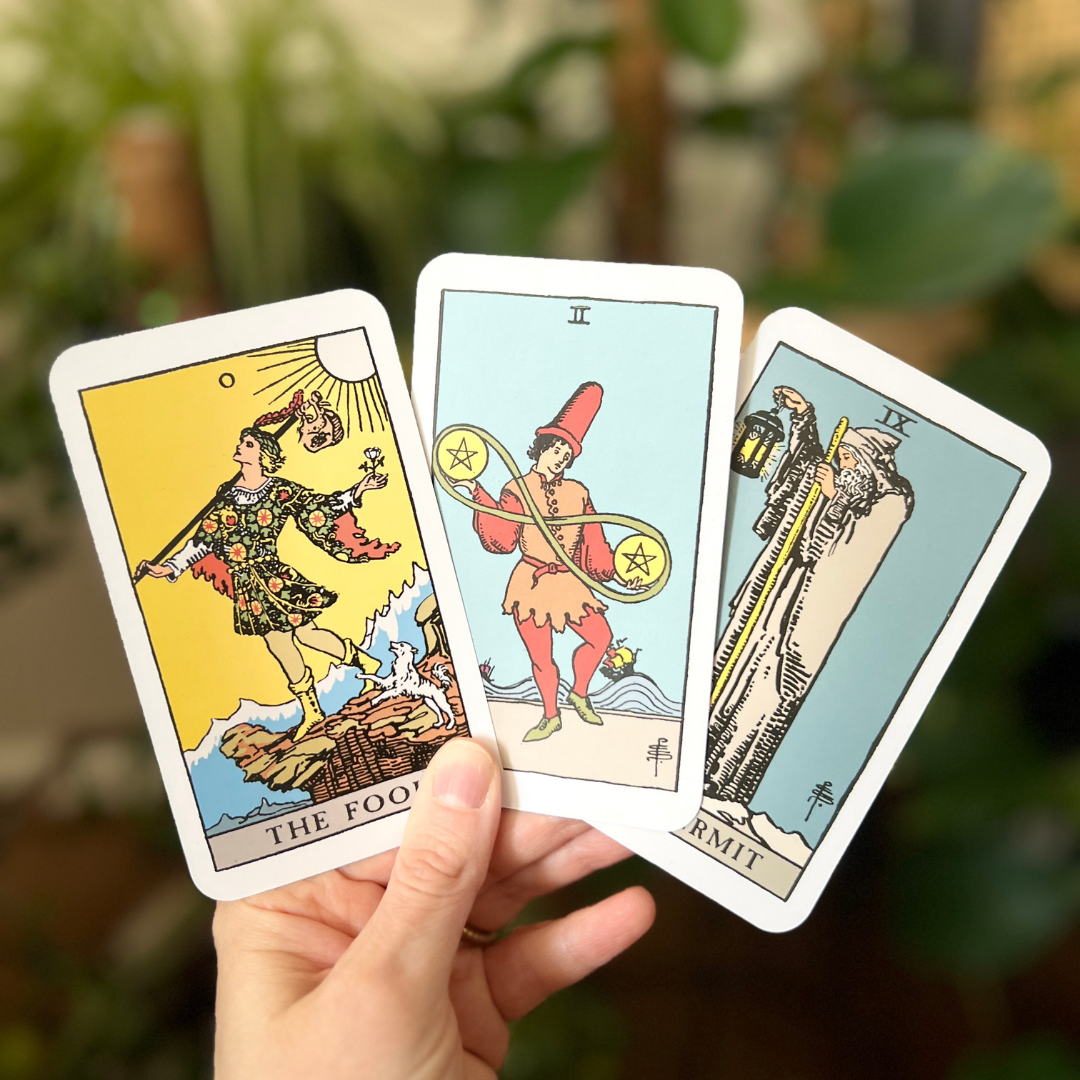 Three Rider-Waite tarot cards (The Fool, Two of Pentacles, and The Hermit) held in hand, representing a beginner’s personal tarot practice focused on reflection and self-inquiry