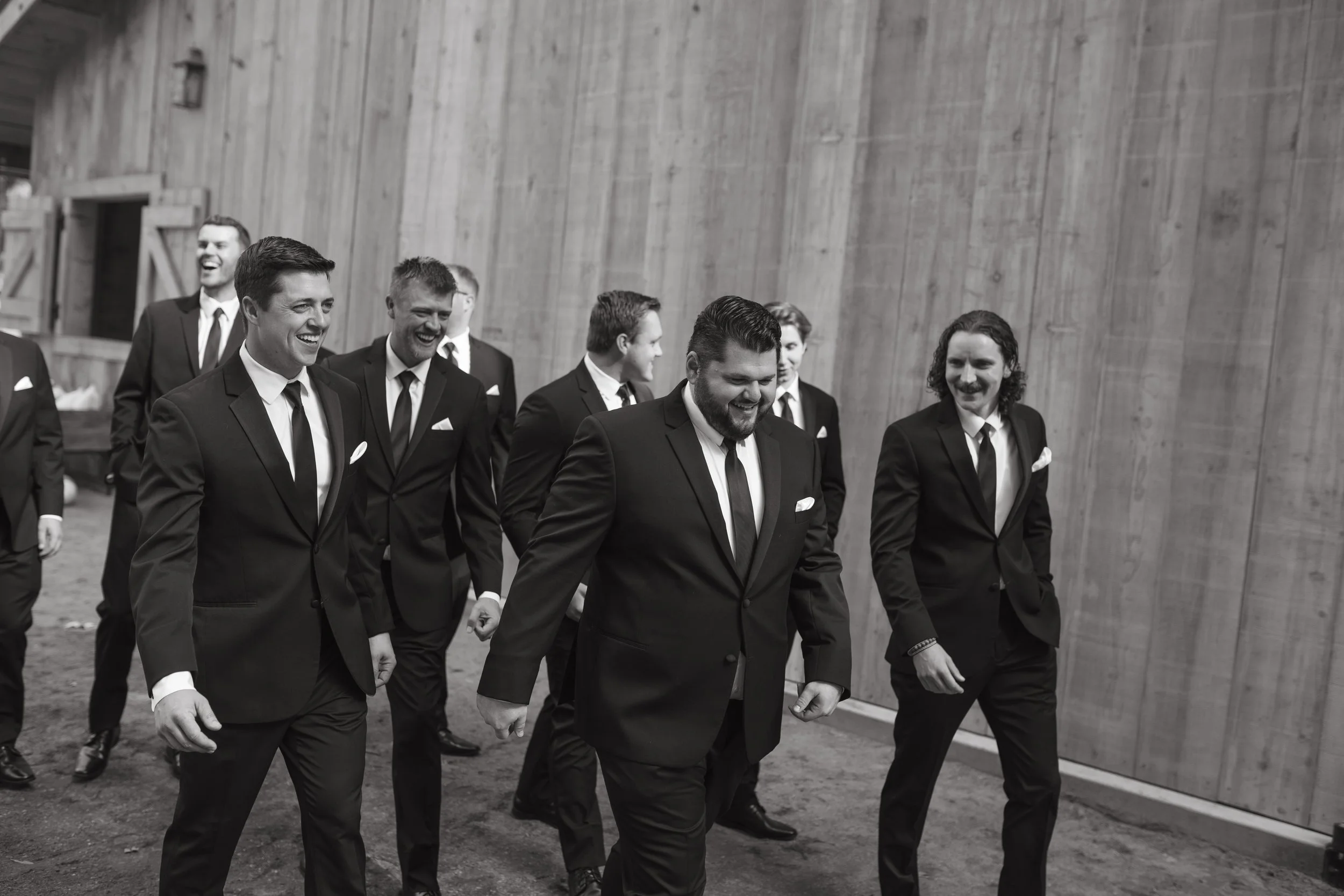 A group of men in suits walking together indoors, smiling and laughing