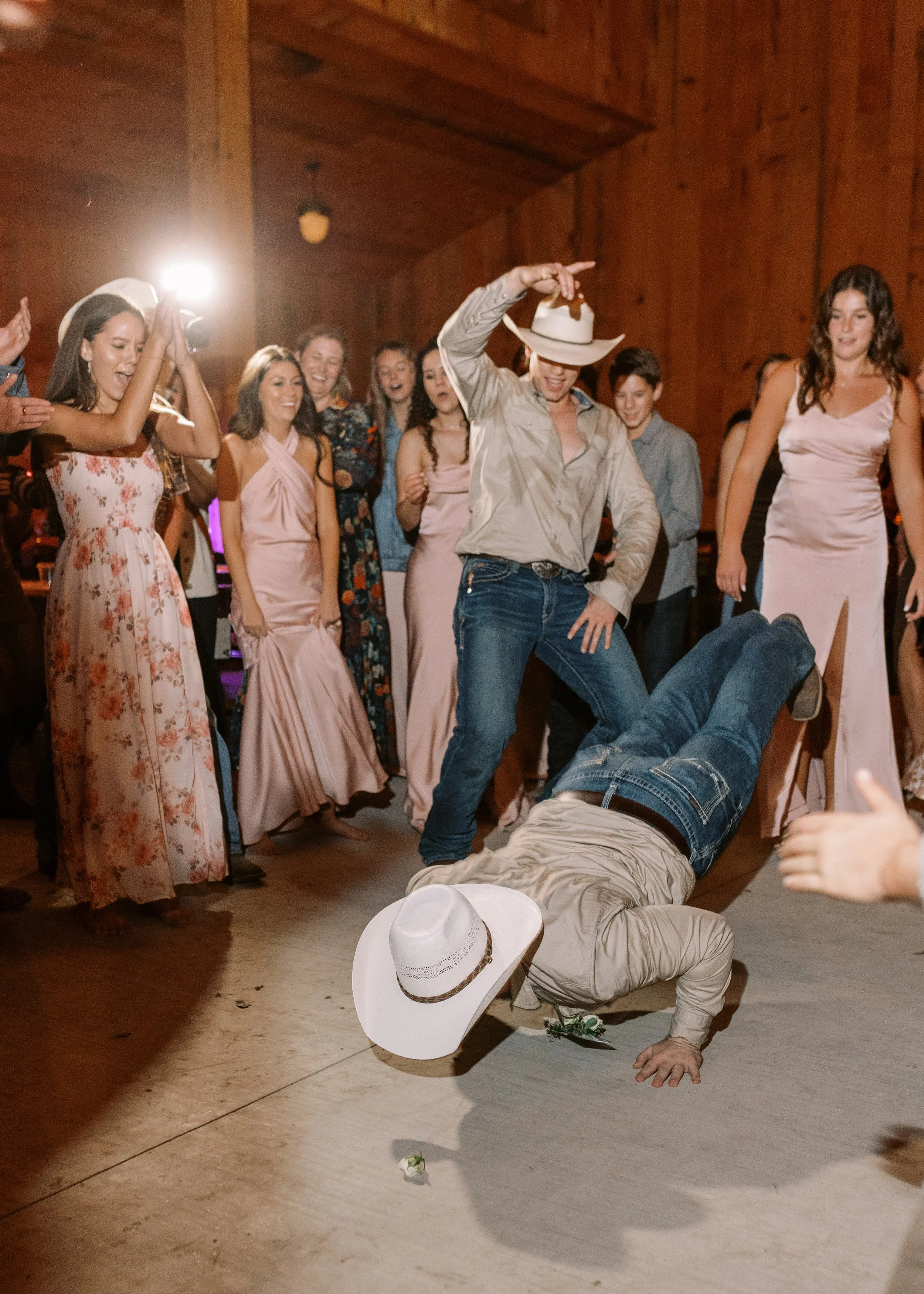 People dancing and celebrating at a party, with a woman in a cowboy hat falling on the dance floor and others watching and cheering.