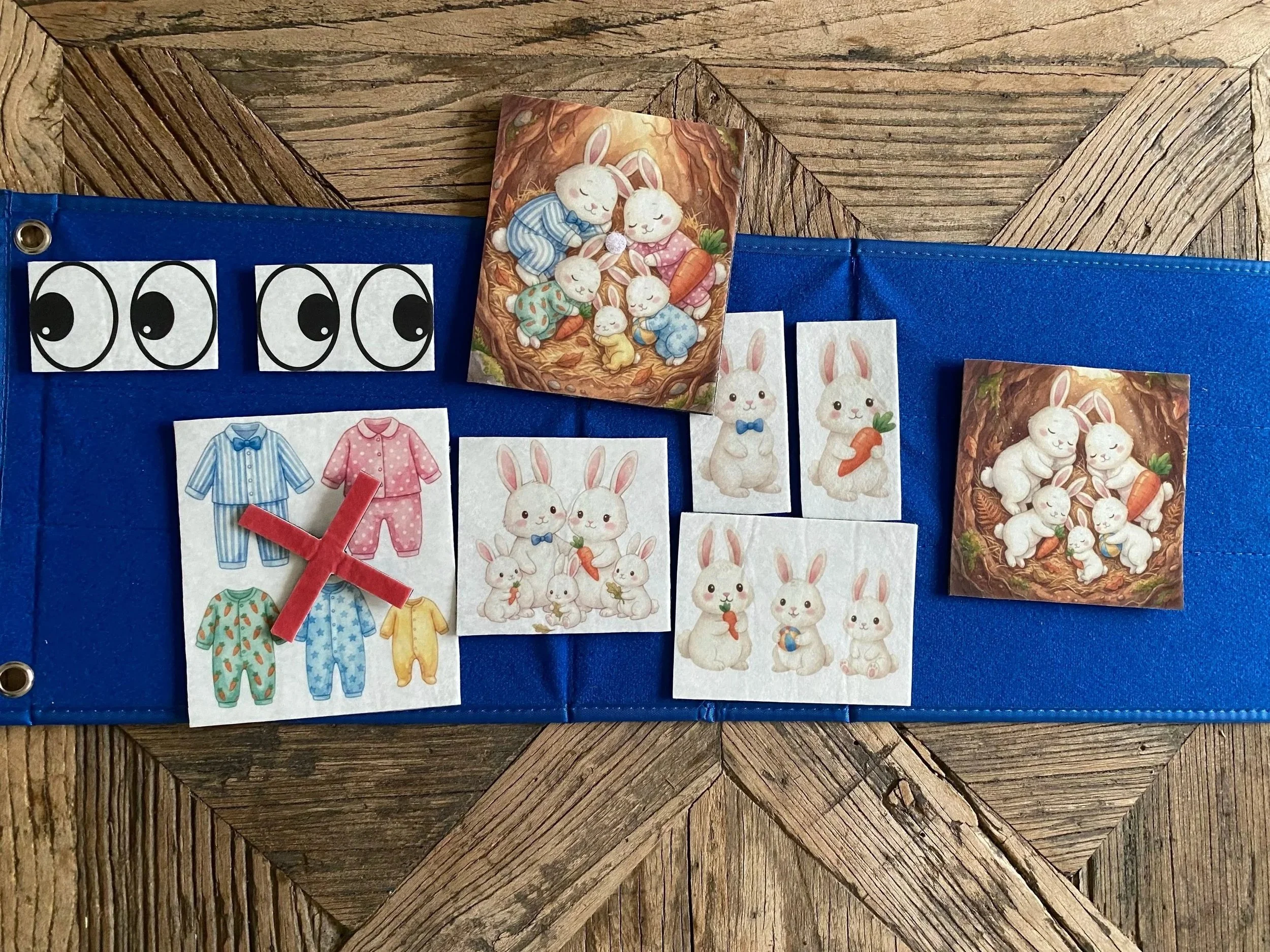 A bulletin board with pictures of rabbits. The top row has illustrations of group of rabbits in nests. The bottom row has images of individual rabbits, some holding carrots, some with party hats, and others with different accessories. There is a fabric with eyes at the top left, and a drawing of pajamas in different styles with a red 'X' placed over some.