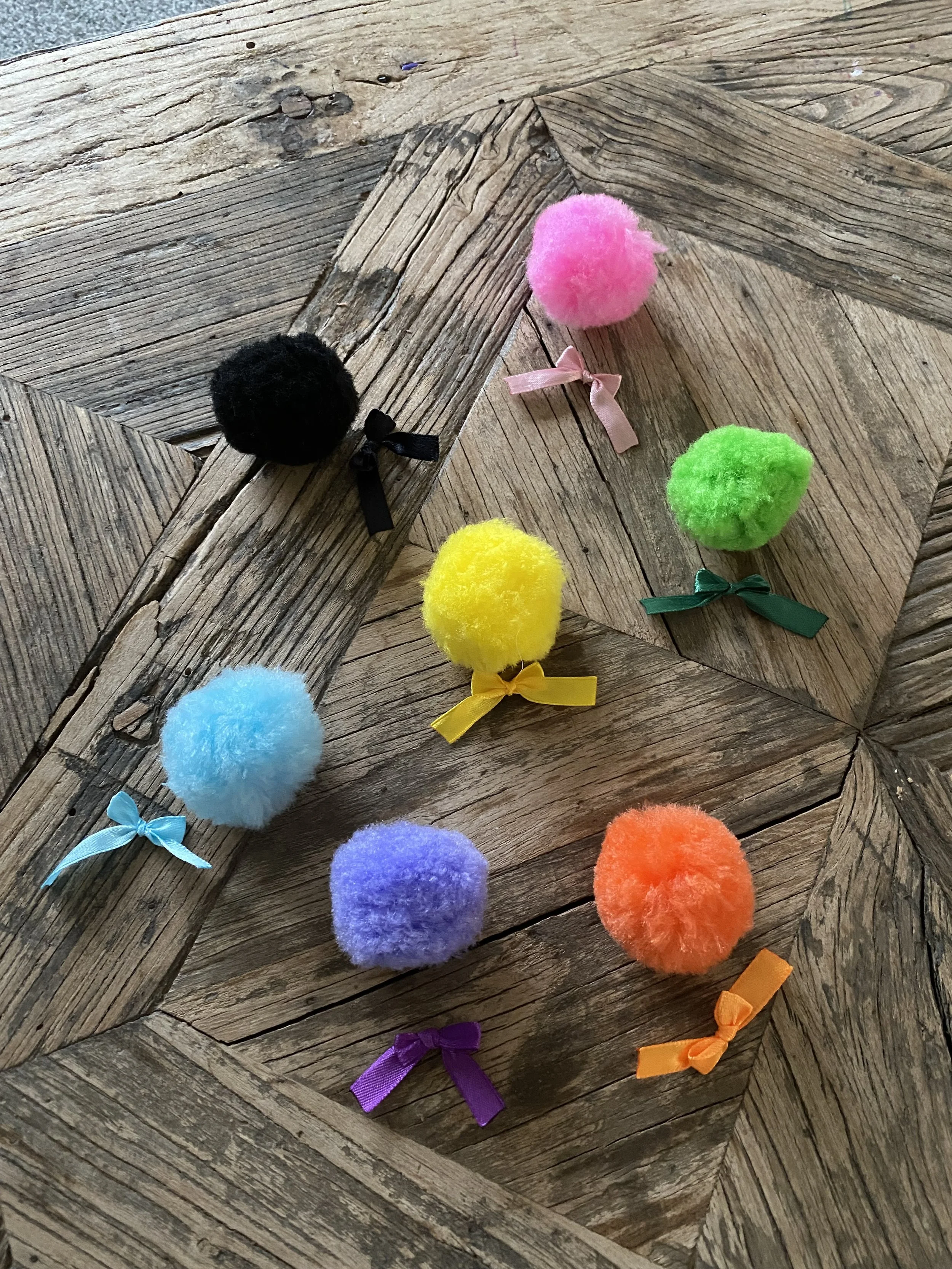 Colorful pom-pom hair accessories with ribbons arranged on a wooden surface.