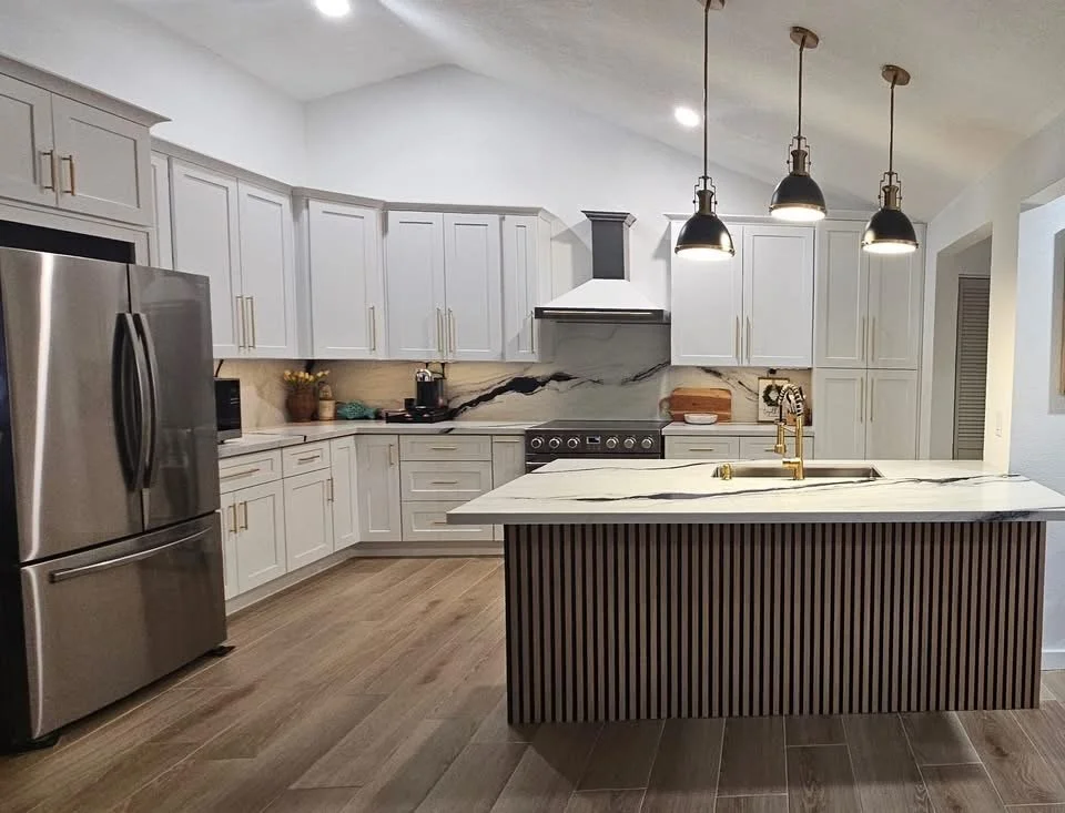 Modern kitchen with white cabinets, stainless steel refrigerator, marble island with striped base, and black pendant lights.