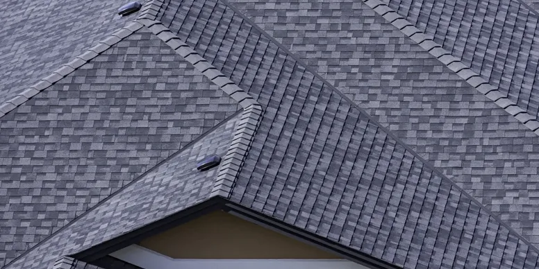 Close-up of a gray shingled roof with a gable and vent pipe.