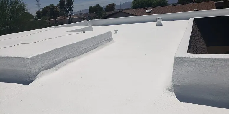 White flat roof with various vents and a parapet wall, under a partly cloudy sky.