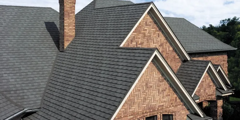 Close-up view of a house's roof with black shingles and brick walls.