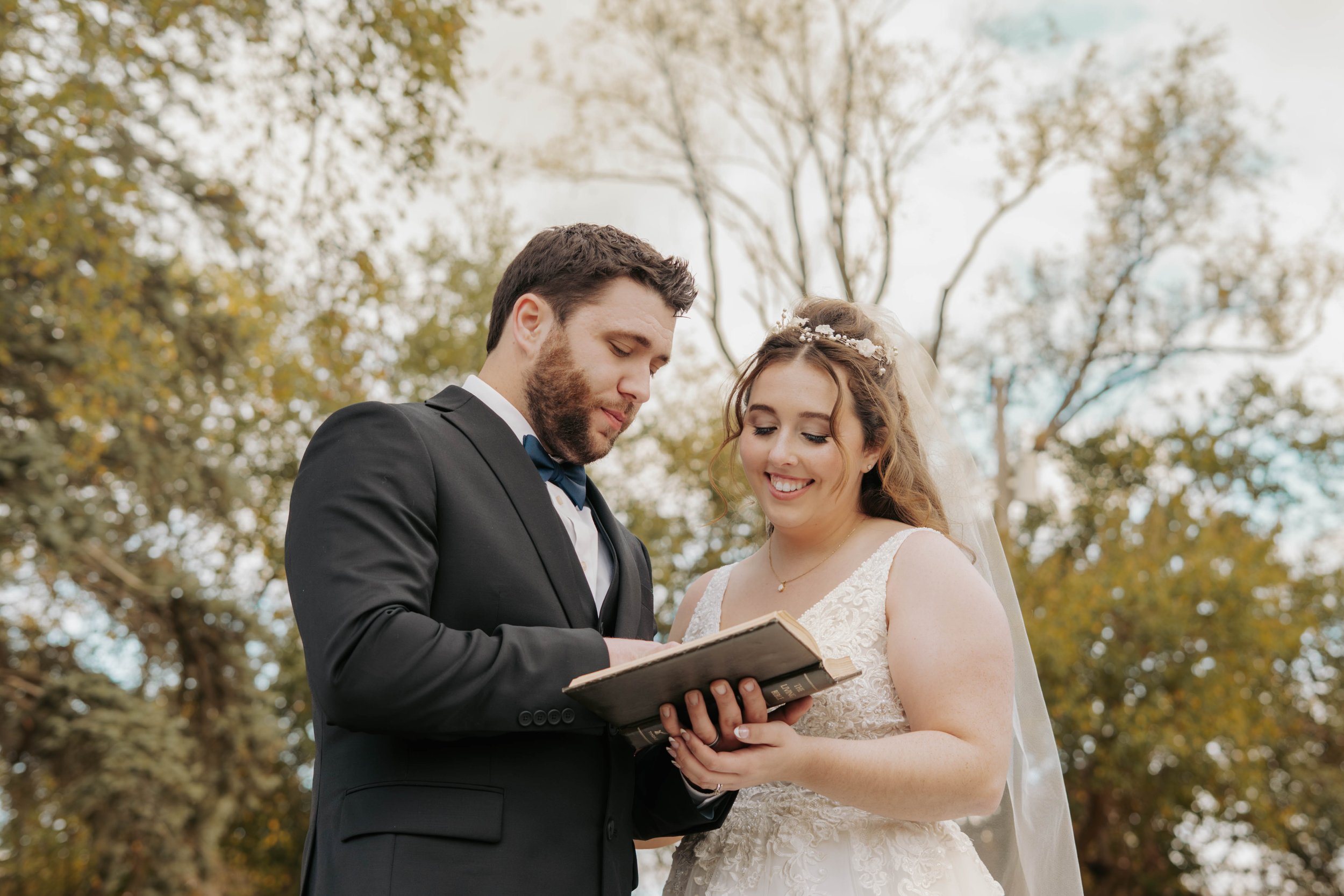 A bride and groom exchanging vows outdoors, holding a book together during a wedding ceremony.