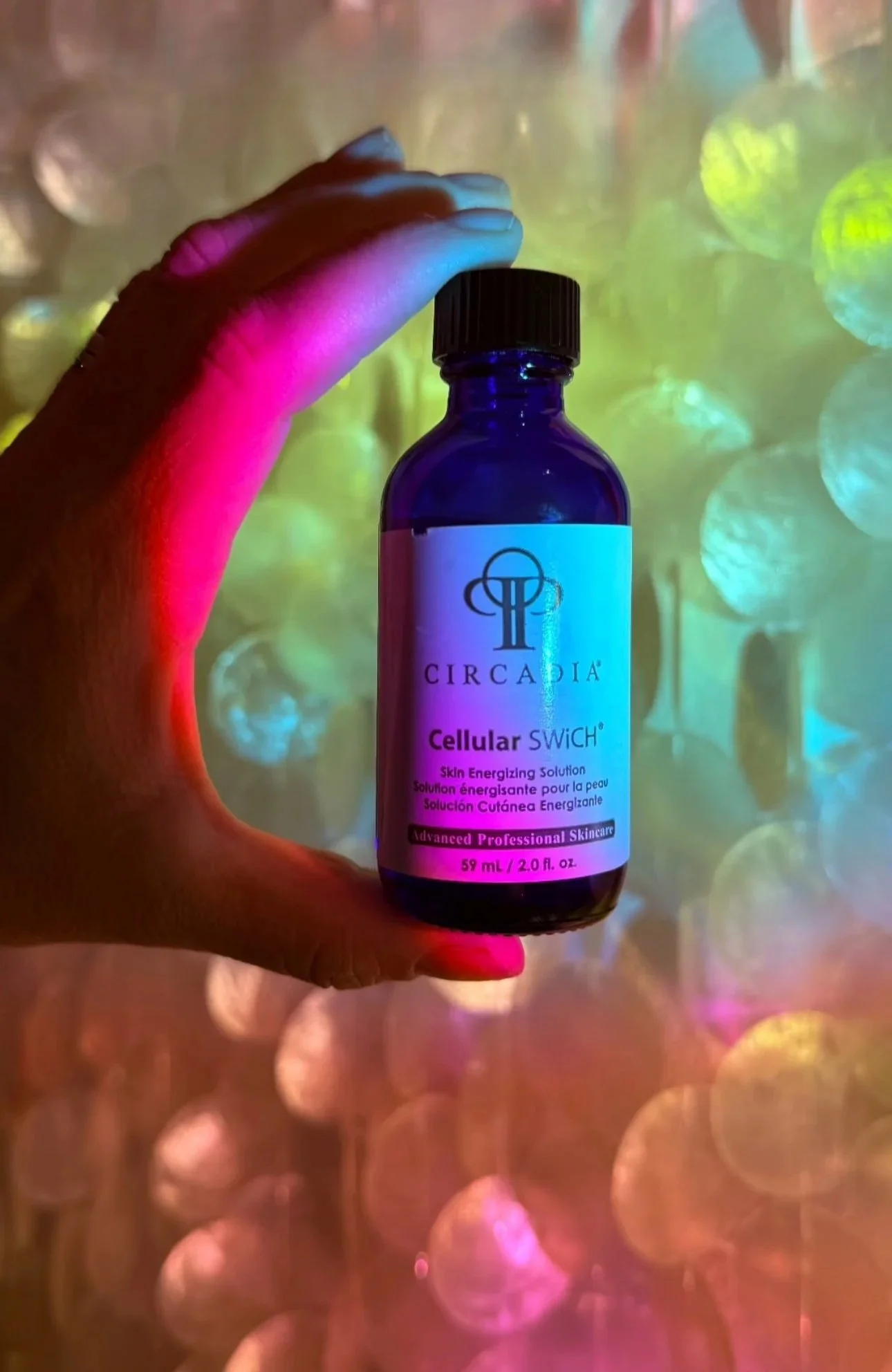 A hand holding a blue bottle labeled 'Circadia Cellular SWiCH' against a colorful, bokeh background.