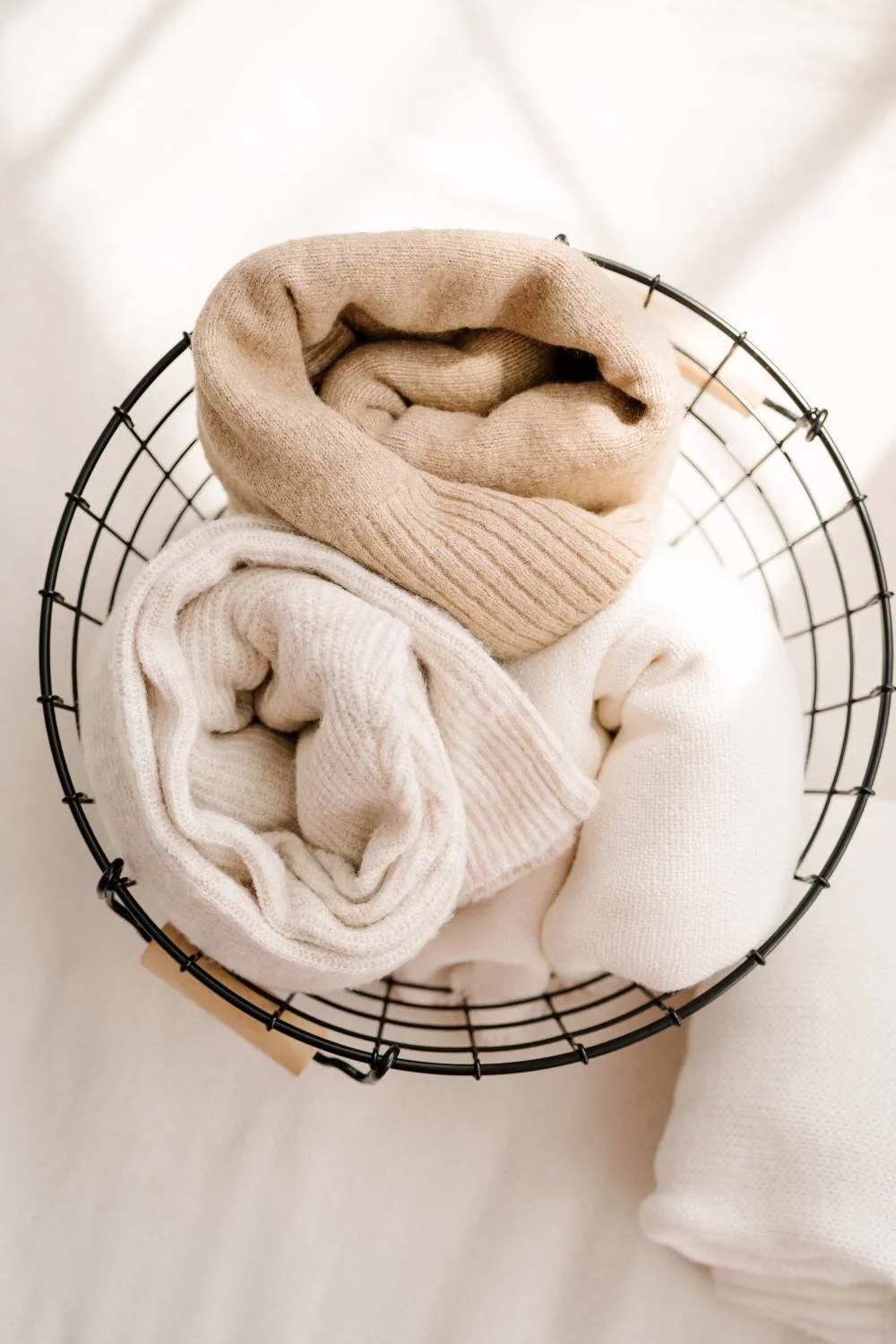 A wire basket containing neatly rolled beige and white sock-like clothing items.
