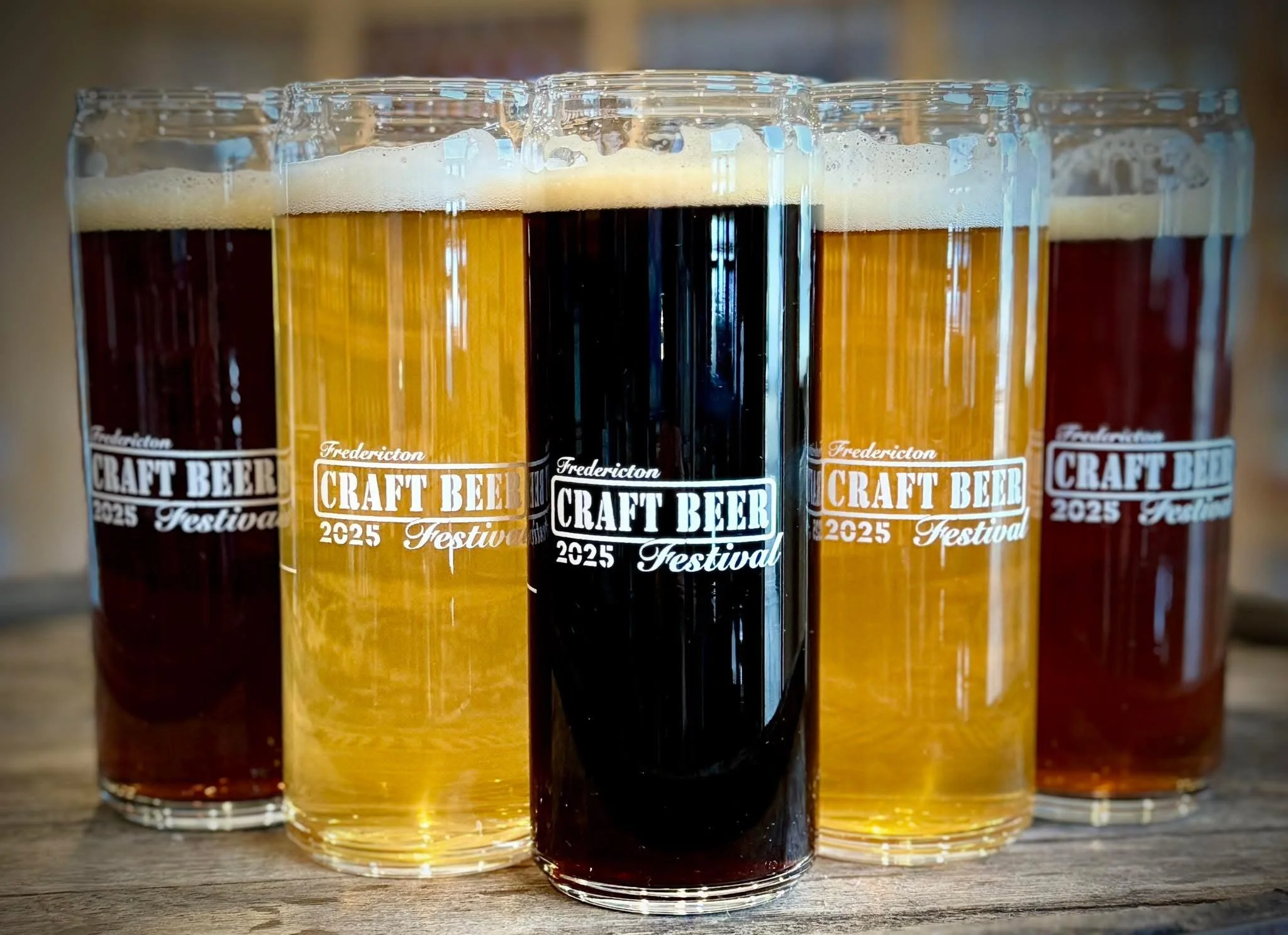 Five craft beers in tall glasses with foam on top, arranged on a wooden surface at the Frederickton Craft Beer Festival 2025.