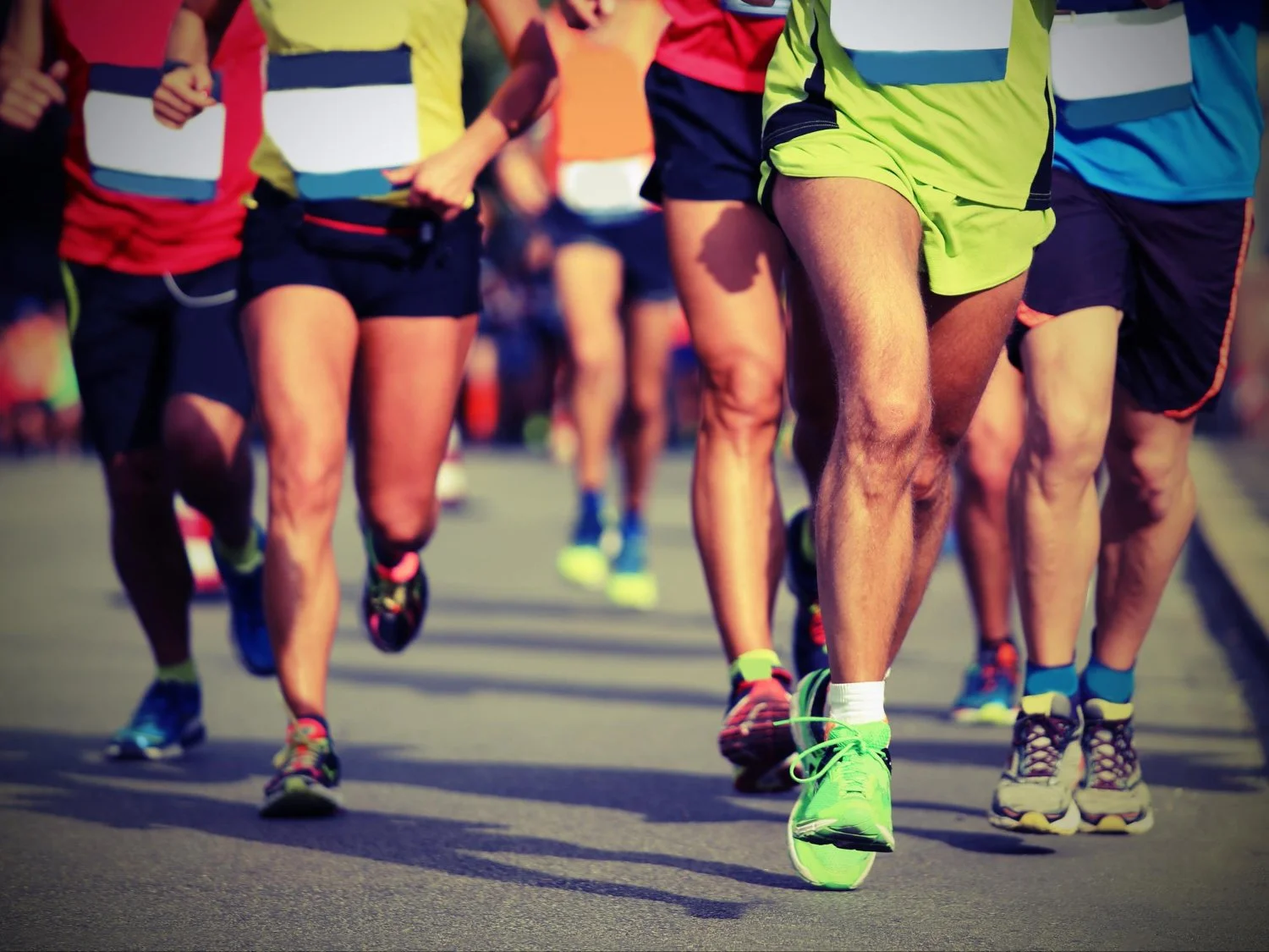 Group of runners participating in a race, wearing athletic clothing and running shoes on a paved road.
