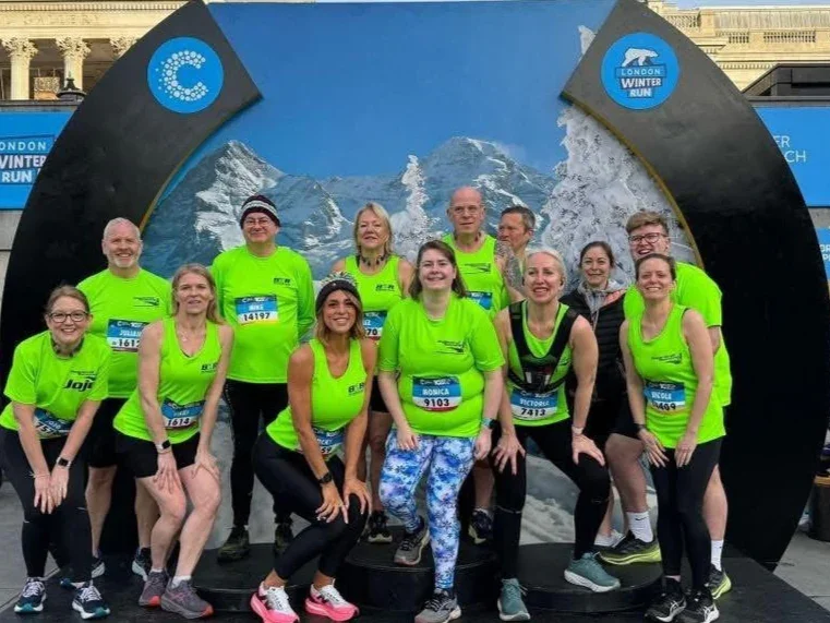 Group of runners in neon green club tops posing in front of a mountain and snow-themed backdrop at the London Winter Run event.