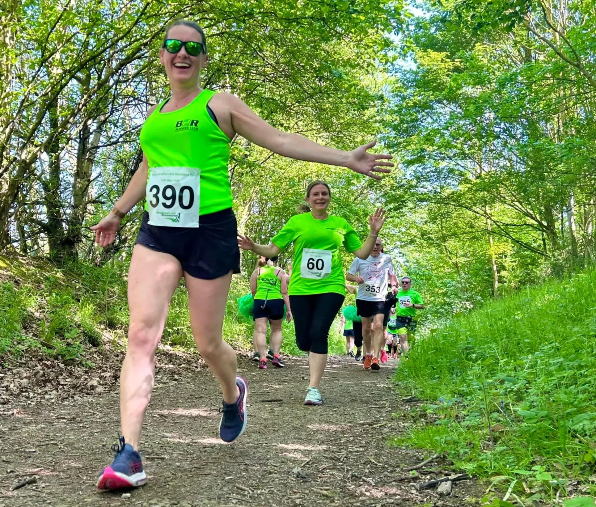 Group of people running in a trail race through a forested area, wearing bright green shirts and race bibs.