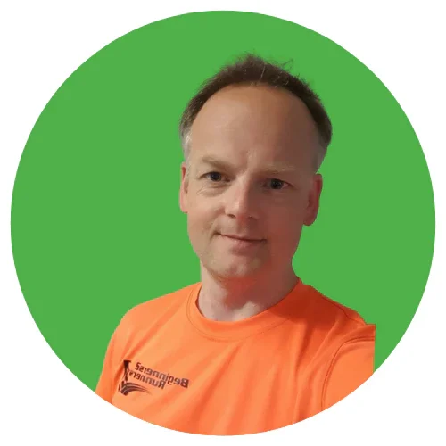 A man with short hair wearing an orange club top, standing in front of a green screen background.