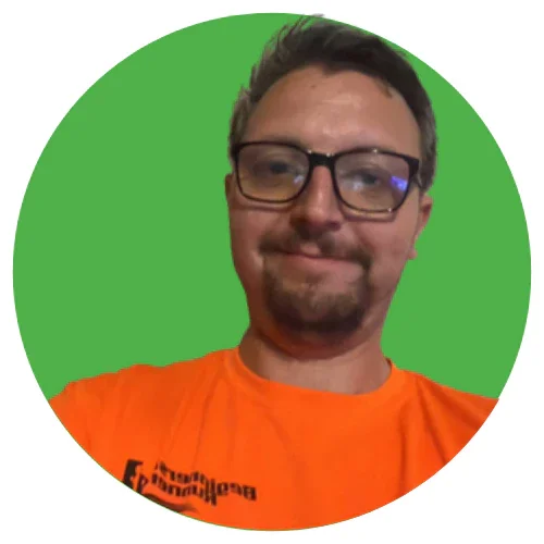 A man with glasses smiling, wearing an orange club top, with a green background.