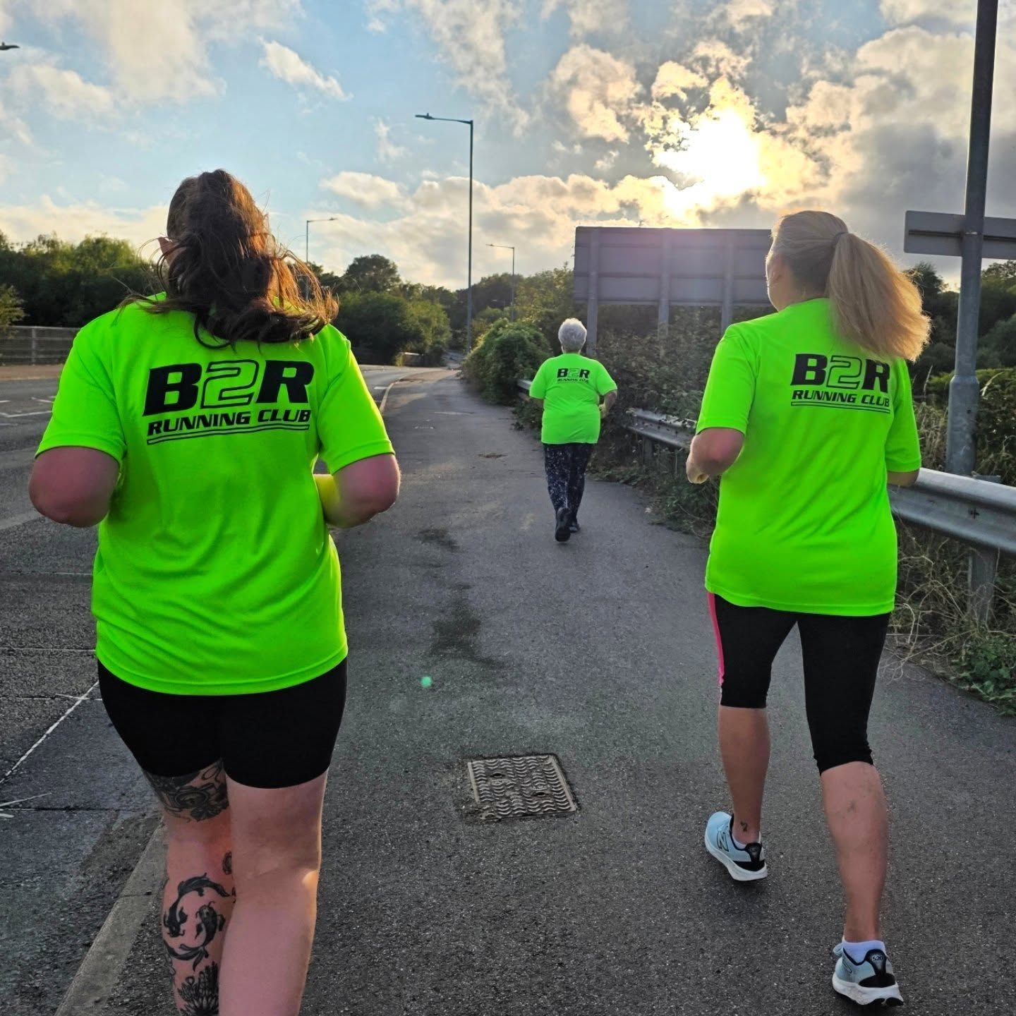 Three women running outdoors on a paved trail during sunset, wearing bright green B2R club tops