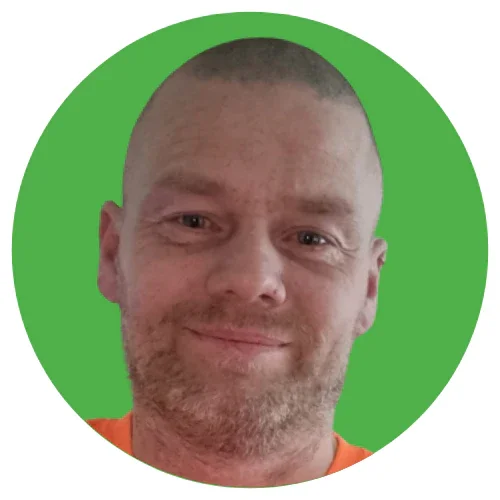 Close-up of a smiling man with short hair and a beard against a green circular background.