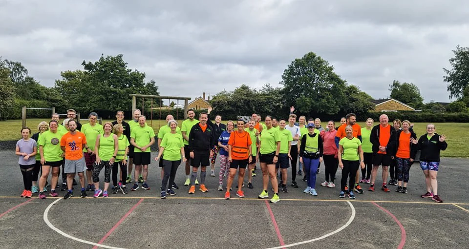 Group of people, mostly in bright running clothes, gathered outdoors on a sports court for a group photo.