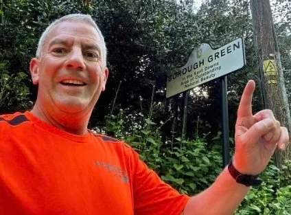 Man taking a selfie outdoors next to a sign that reads 'Broough Green.'