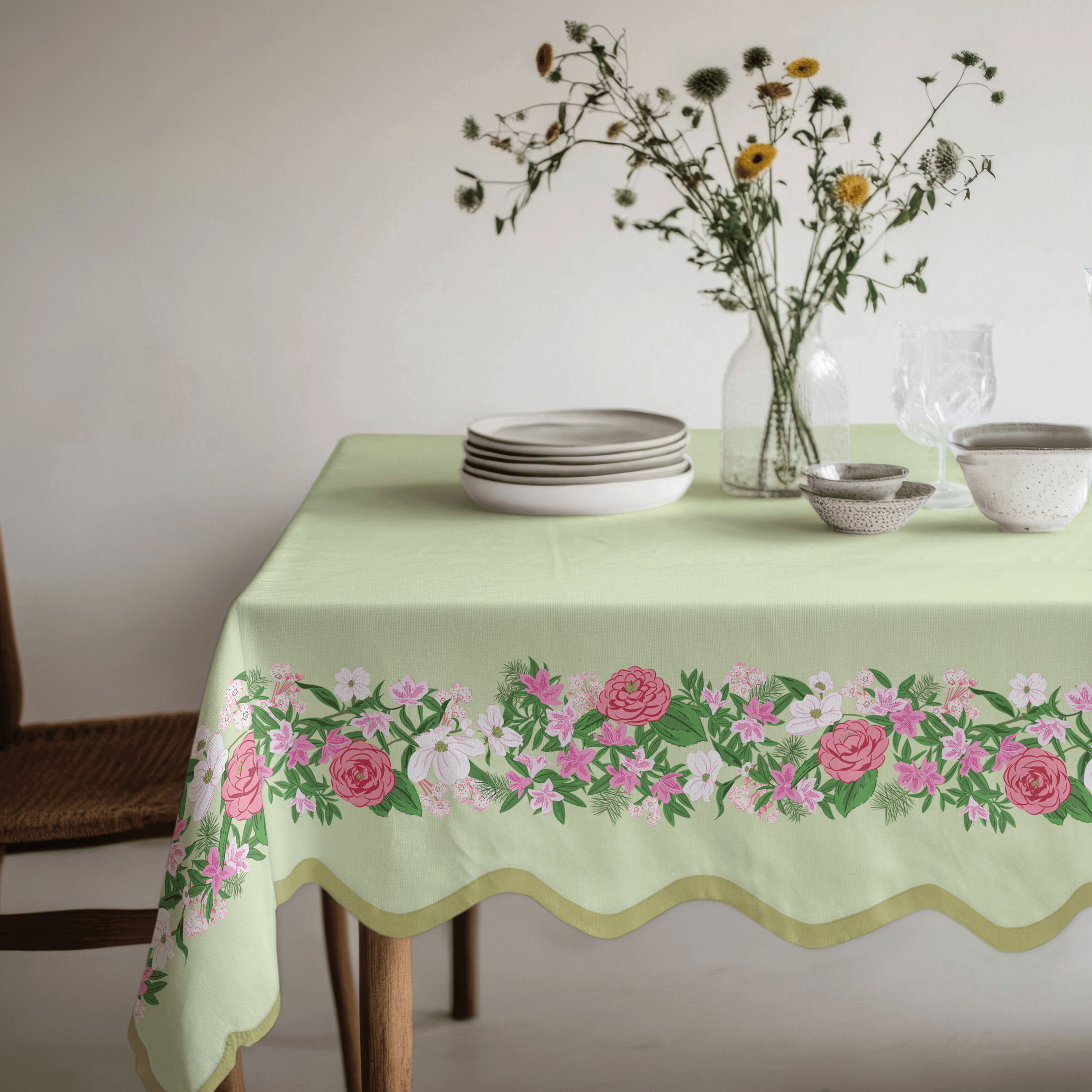 Dining table dressed with a green tablecloth featuring a floral garland border trim along the edge, styled with plates, glassware, and fresh flowers.