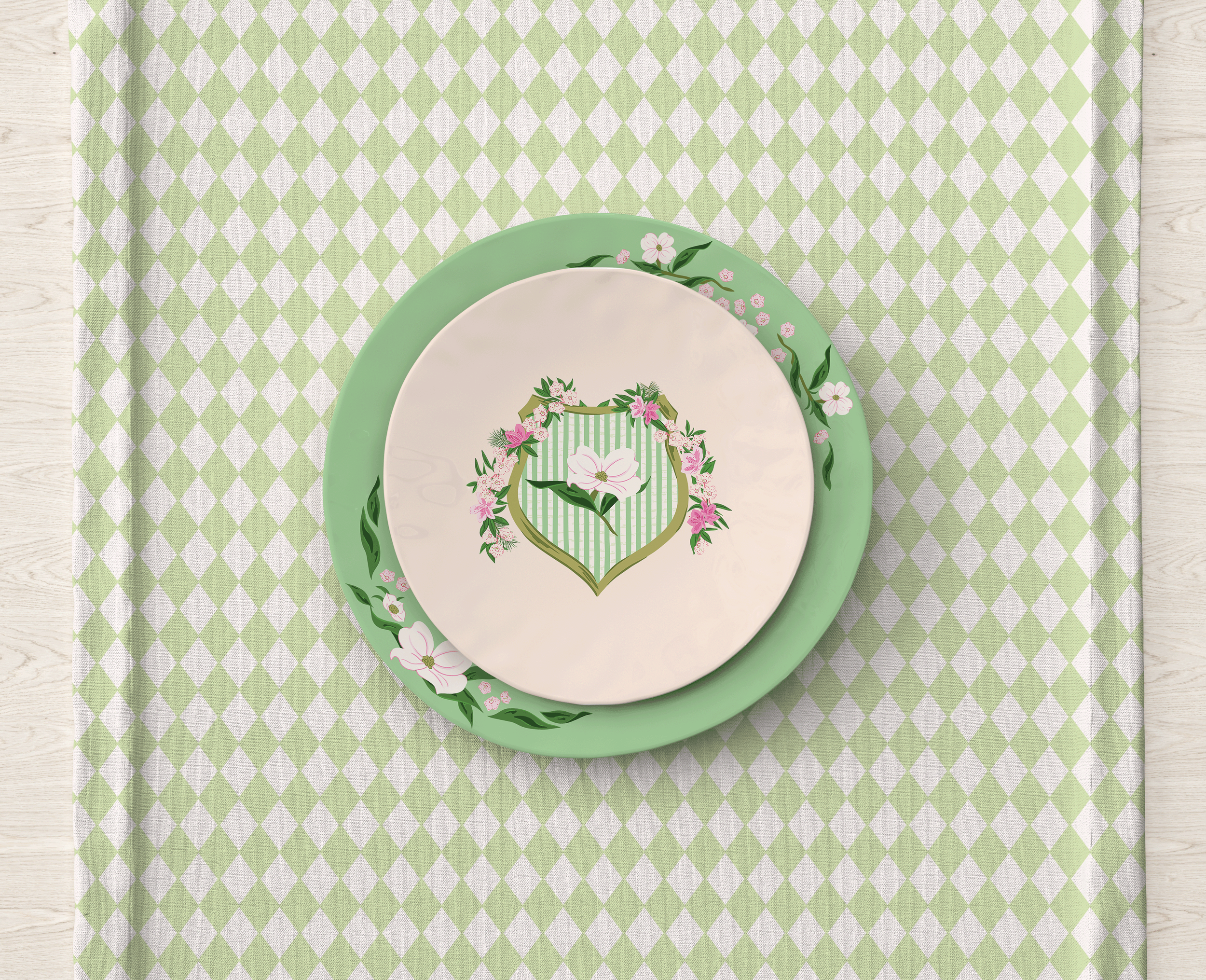 Tabletop place setting featuring a decorative plate with the Lawn League crest centered inside a circular floral border, displayed on a green geometric diamond patterned placemat.