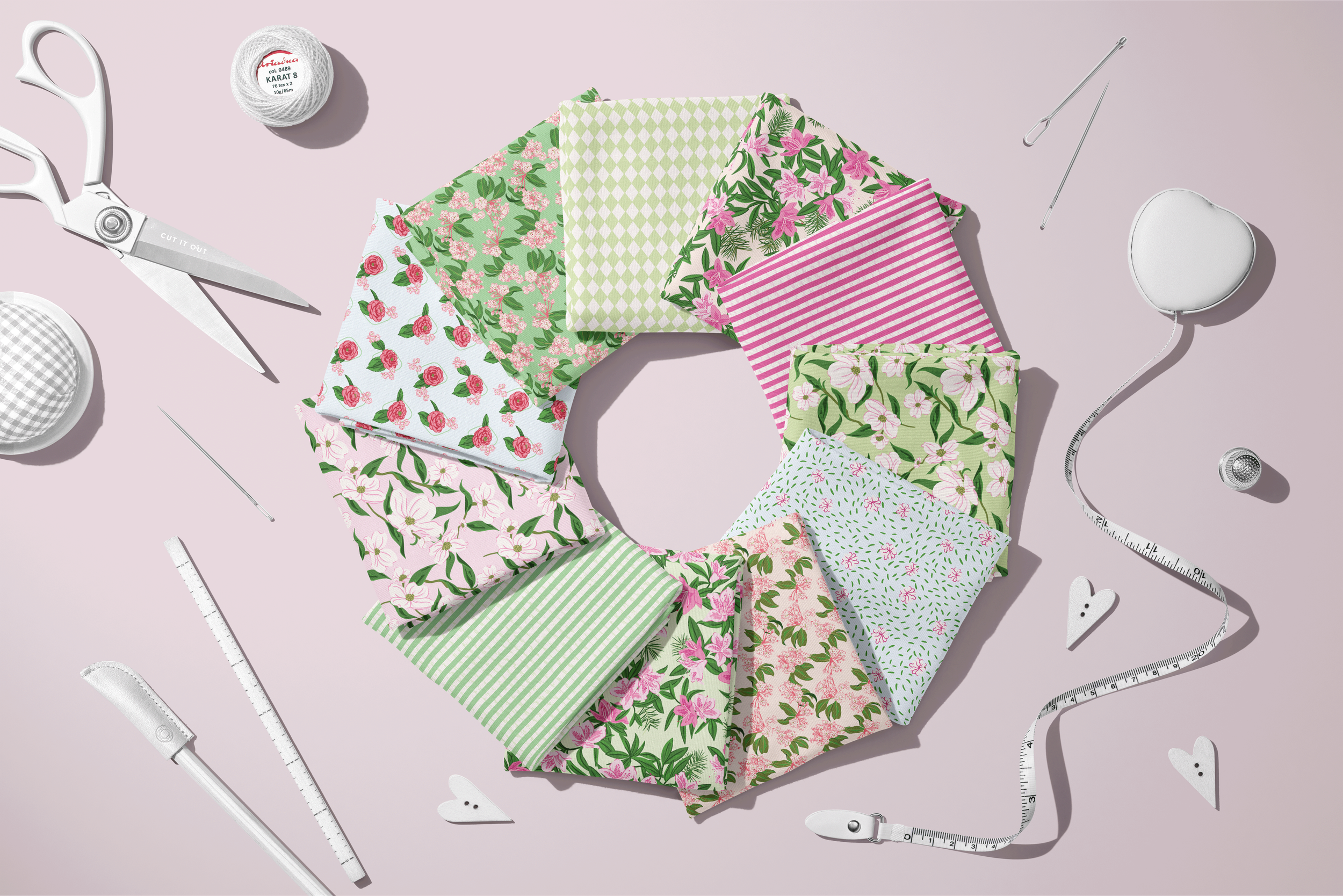 Assortment of coordinating Lawn League fabric swatches arranged in a circle beside sewing tools, showcasing floral, striped, geometric, and blender patterns in pink and green.