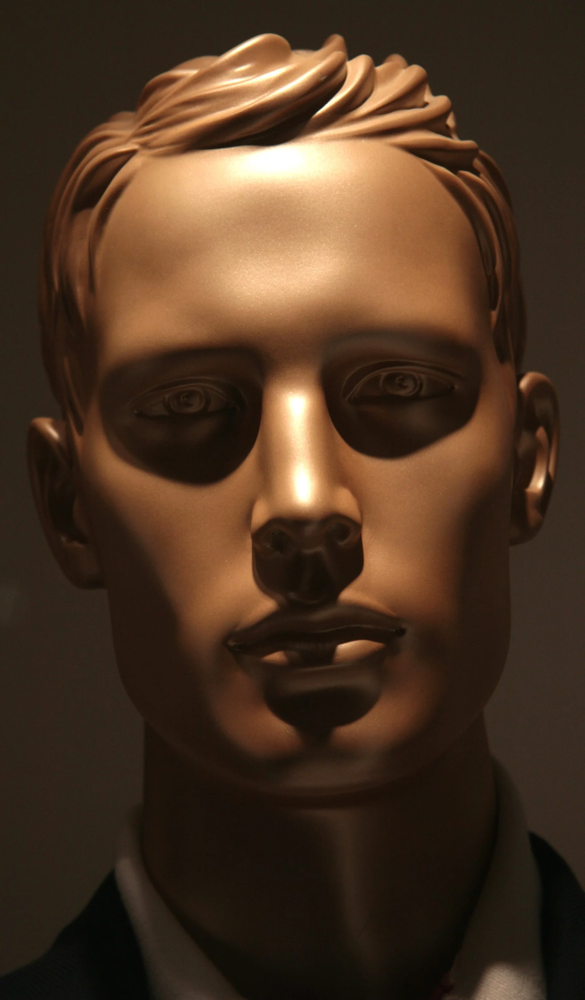 Portrait d'un homme en bronze avec des détails réalistes, portant un costume noir et une chemise blanche.