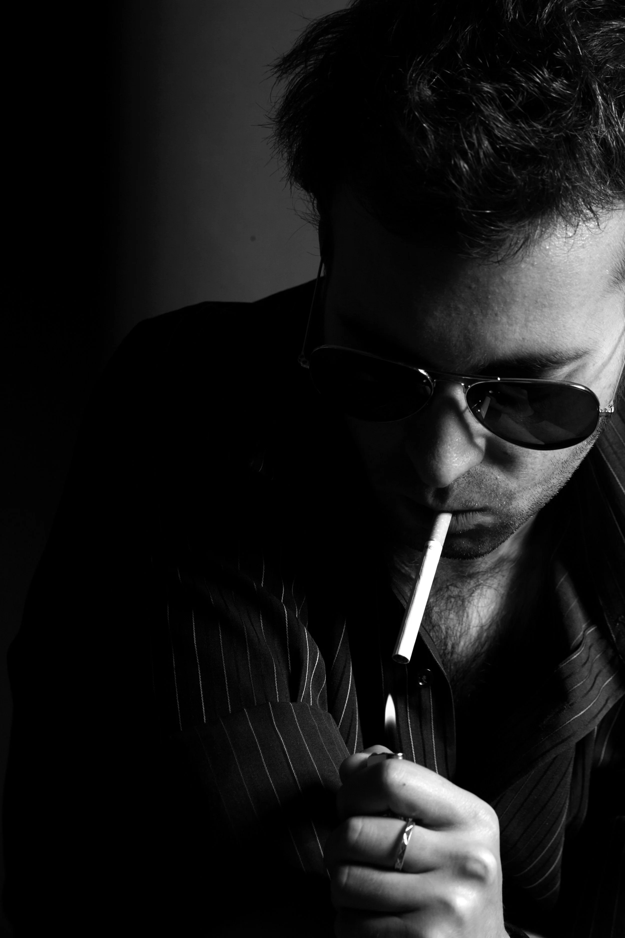 Un homme portant des lunettes de soleil, fumant une cigarette et tenant un briquet, dans un style sombre en noir et blanc.