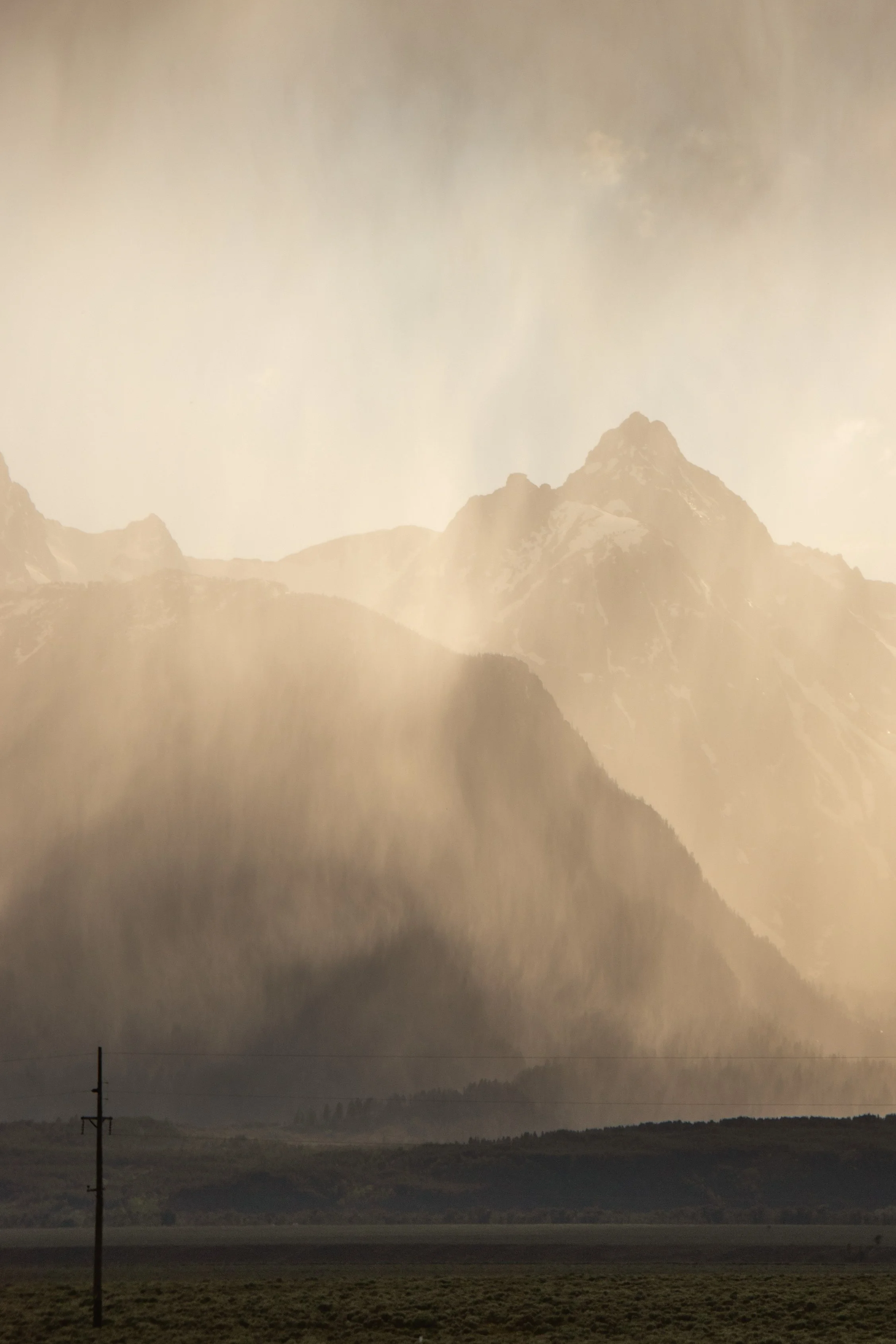 Mountain range with peaks, some snow-capped, and a foggy or misty atmosphere. Foreground shows flat land with a single utility pole.
