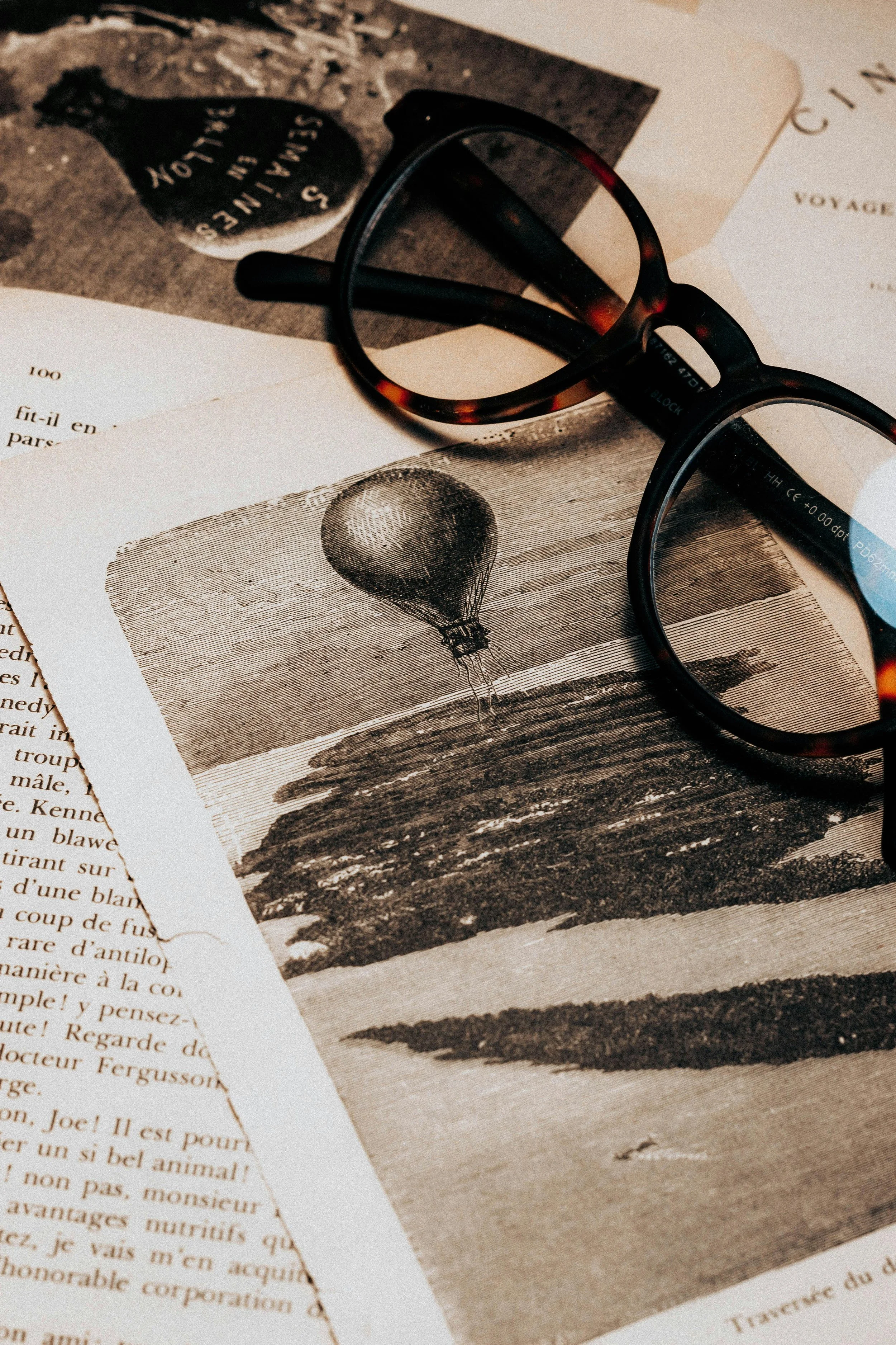 A pair of black glasses resting on vintage papers, including a photo of a hot air balloon flying over a landscape.