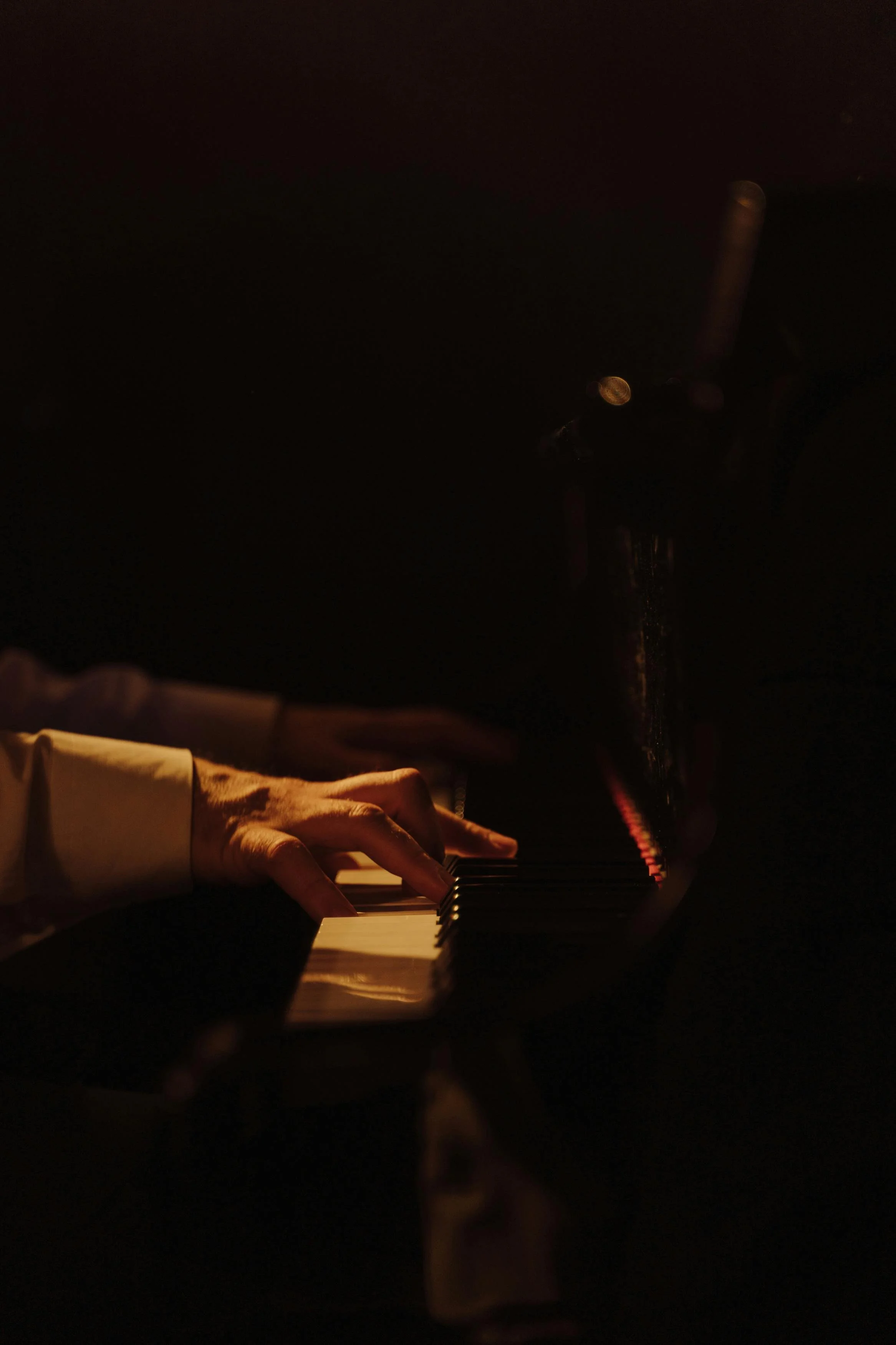 A person playing a piano in a dark environment with soft, warm lighting highlighting their hands on the keys.