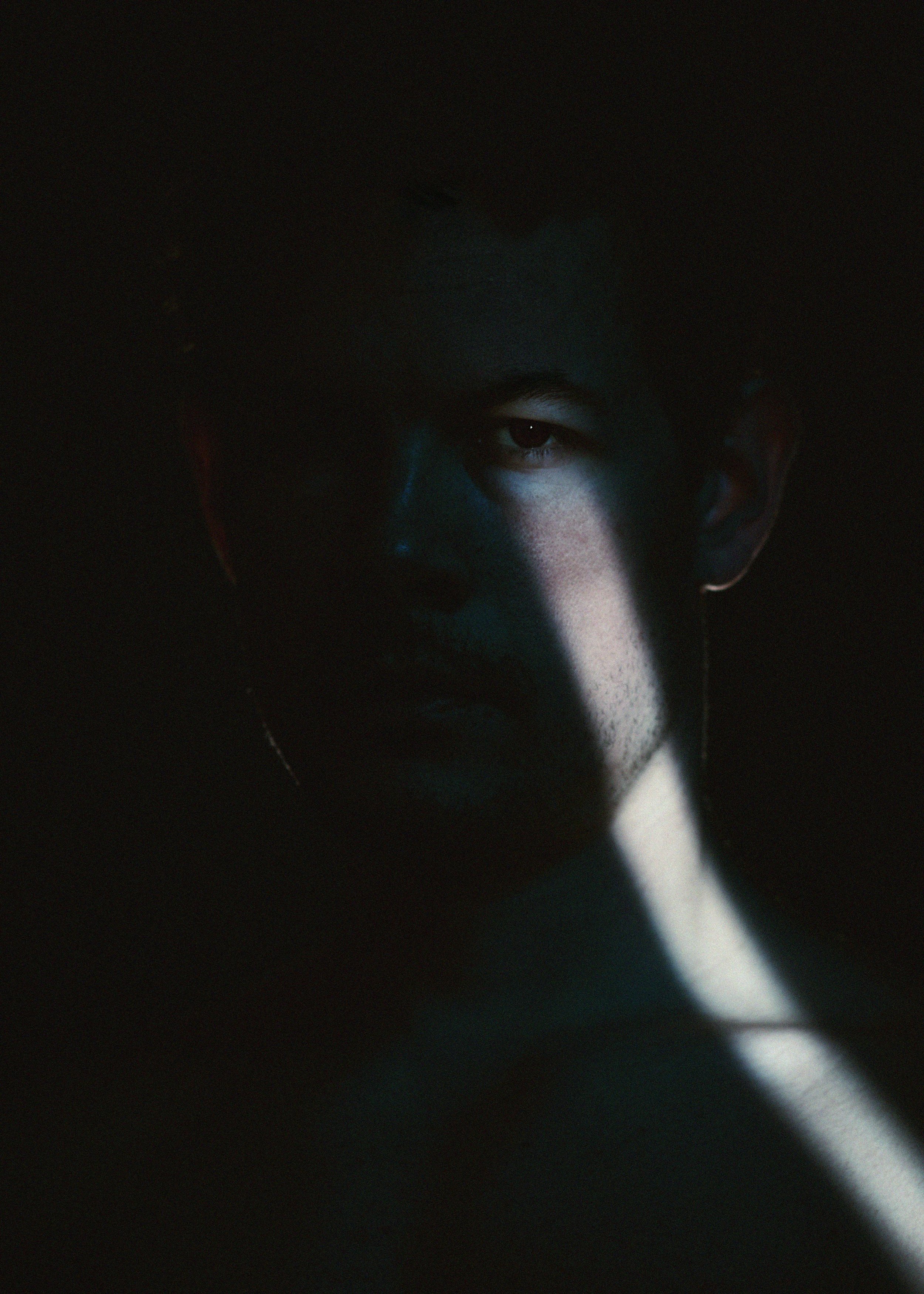 A person's face partly illuminated by a beam of light in a dark setting.