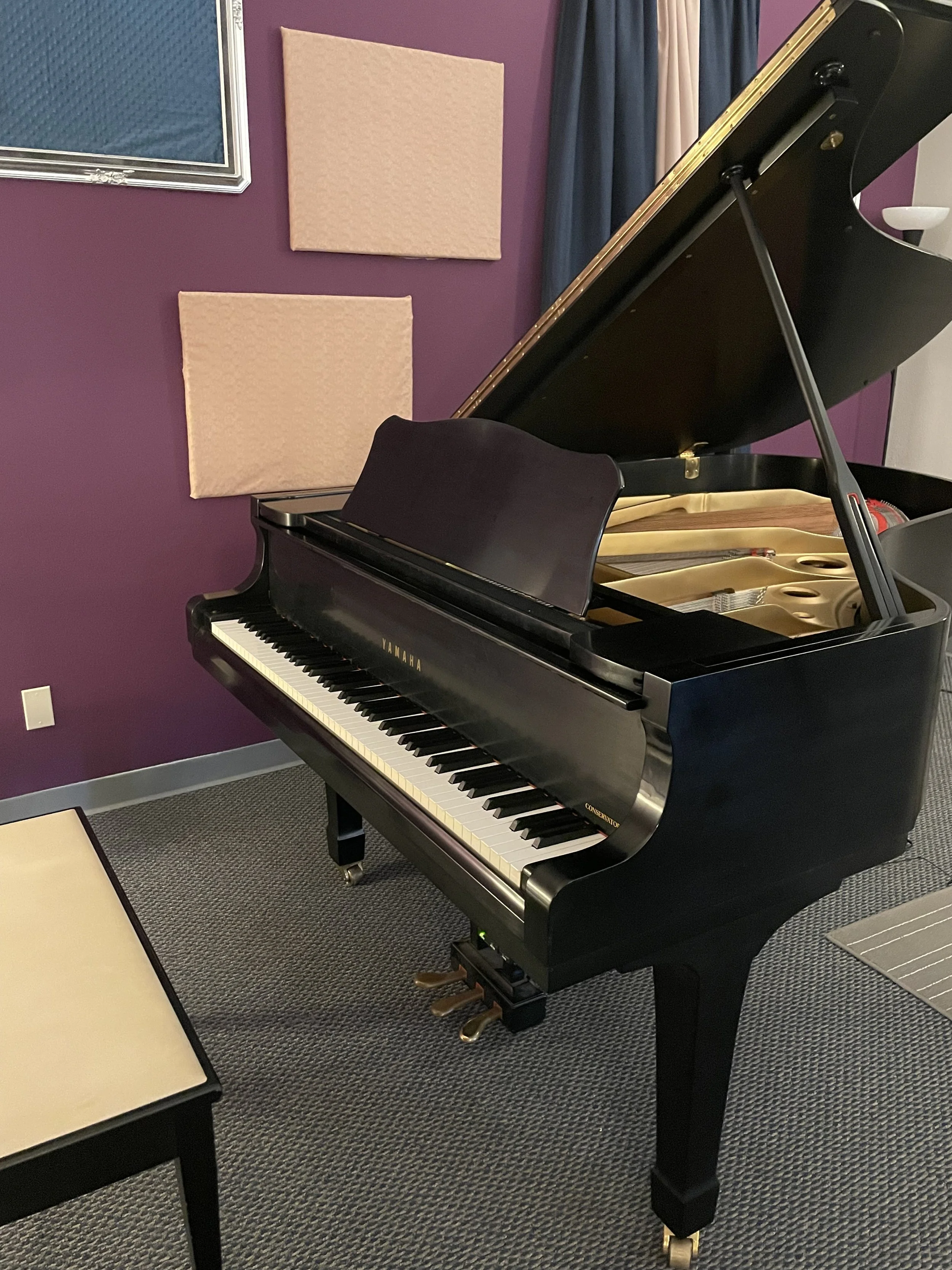 Black grand piano with open lid in practice room with purple walls and soundproofing panels.