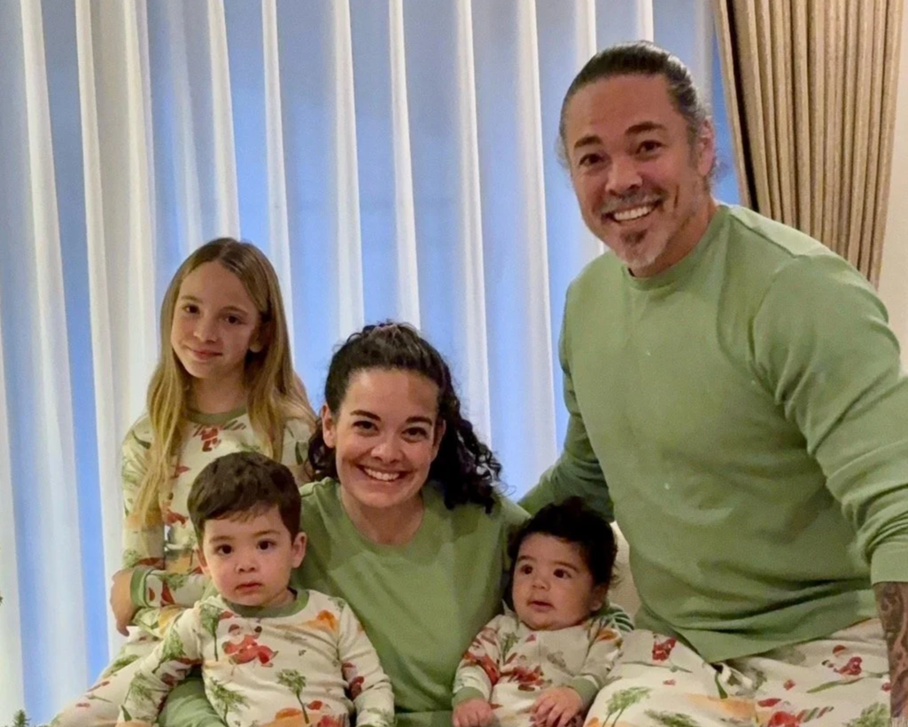 Family of five, including two young girls and two young boys, gathered together indoors, smiling at the camera.