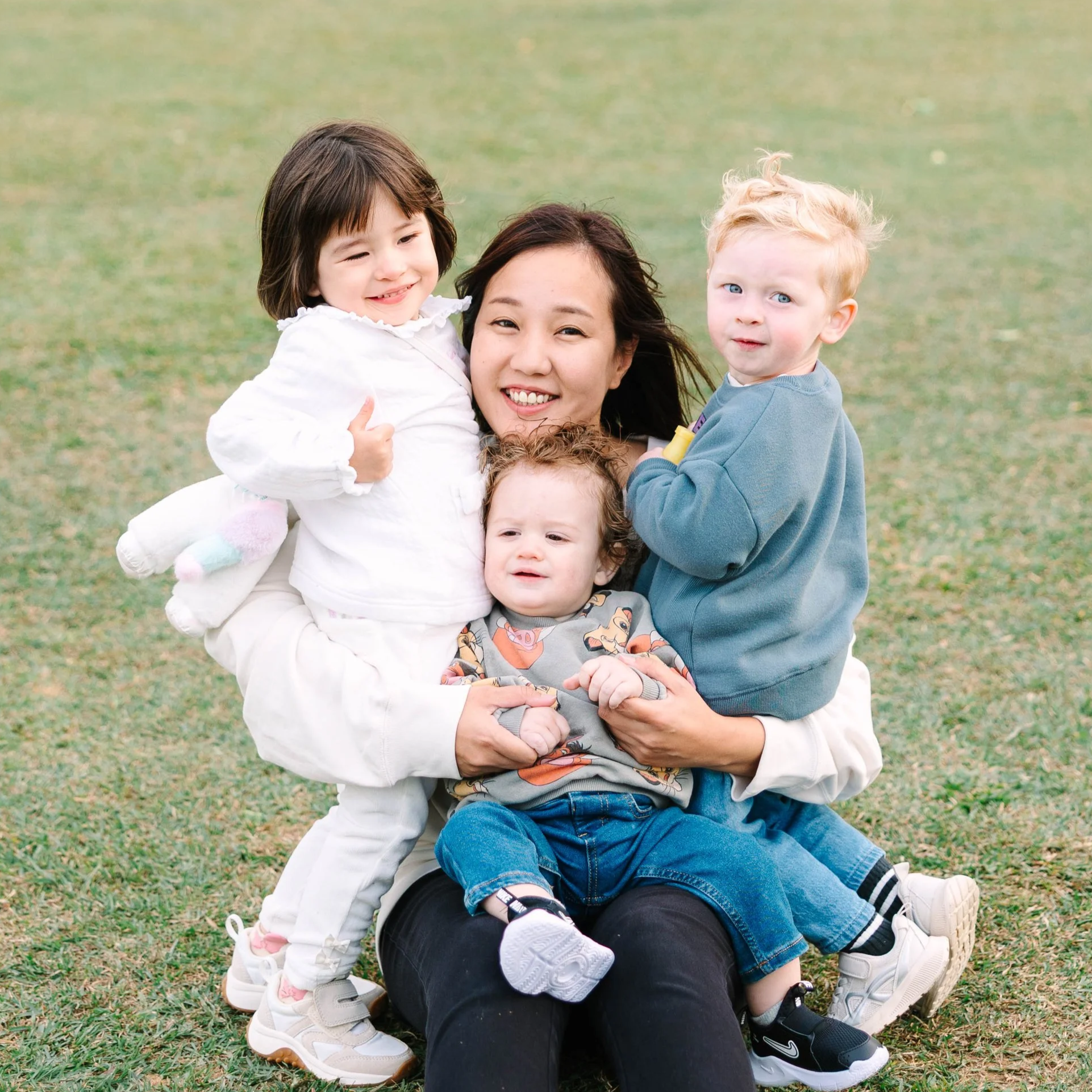 Mother sitting on grass with four children, smiling, outdoor park setting.