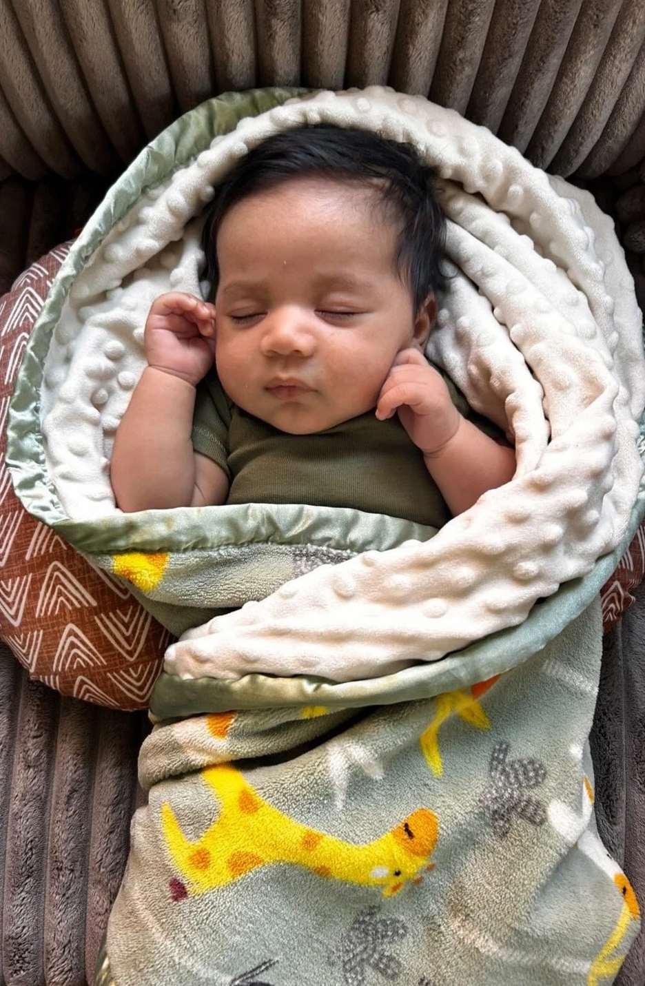 A sleeping baby wrapped in a blanket, lying on a soft surface.