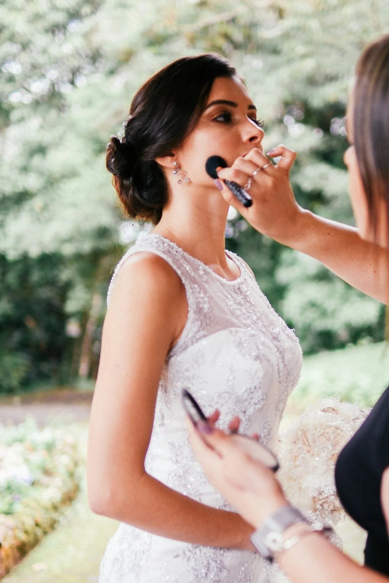 A woman in a wedding dress having her makeup done outdoors.