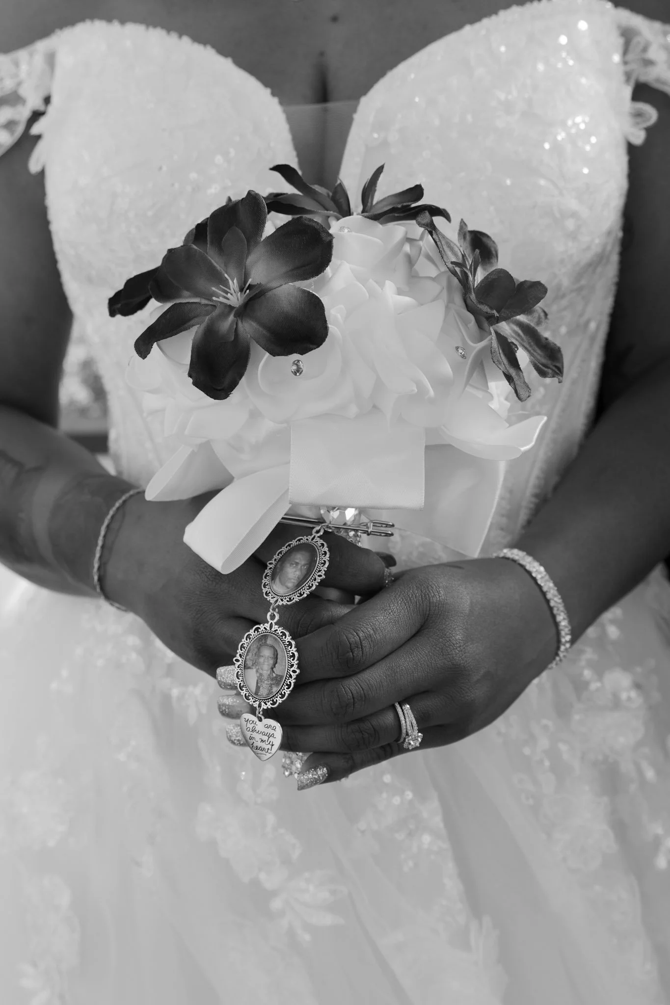 A bride holding a bouquet of flowers, wearing a wedding dress, with jewelry and rings on her hand, in black and white.
