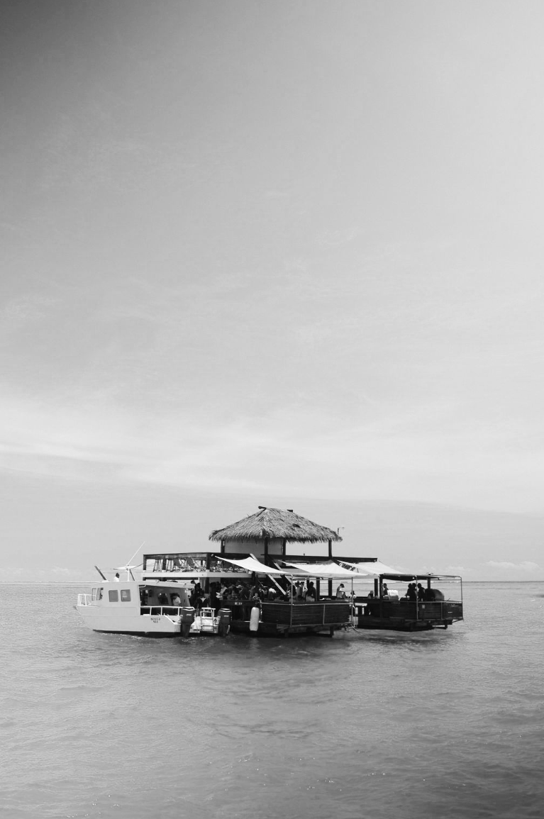 A boat with a thatched roof on the water, featuring an open seating area and people dining or relaxing.