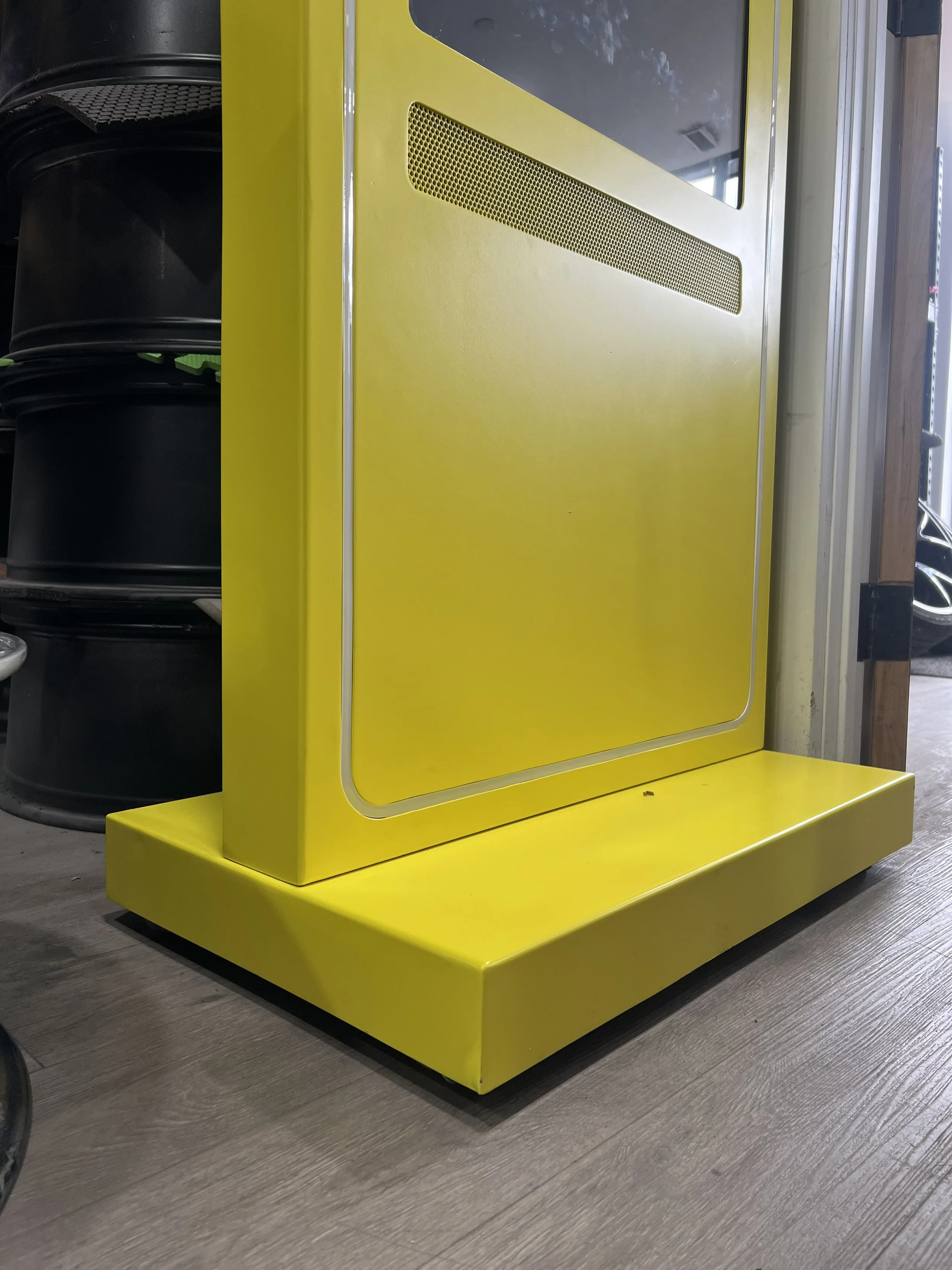 A yellow vintage-style jukebox with a vent and a rounded base, situated on a wood floor in a store or retro setting.