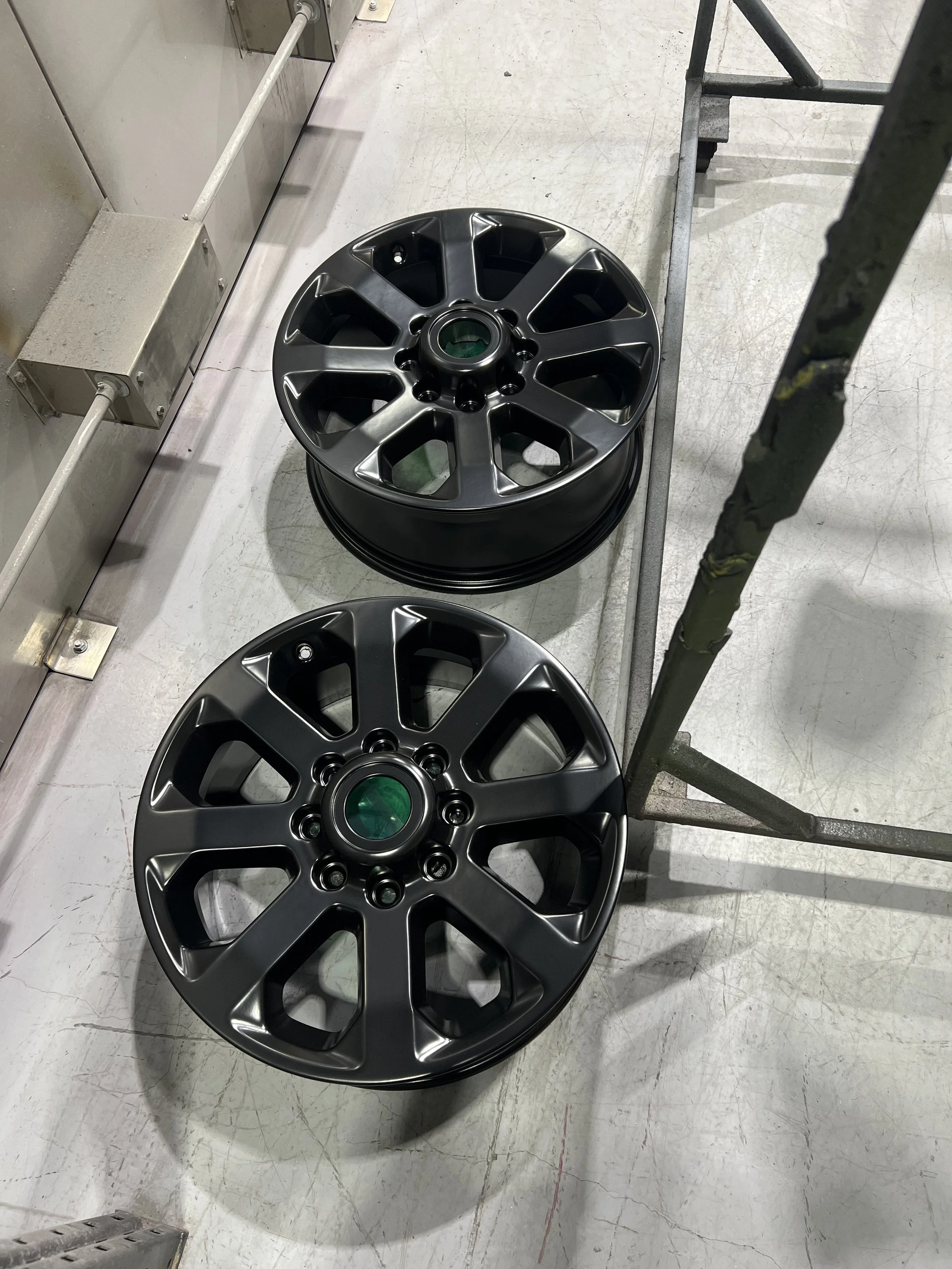 Two black car wheels stacked on top of each other on a light-colored concrete floor, next to a metal scaffold and a metal electrical box.