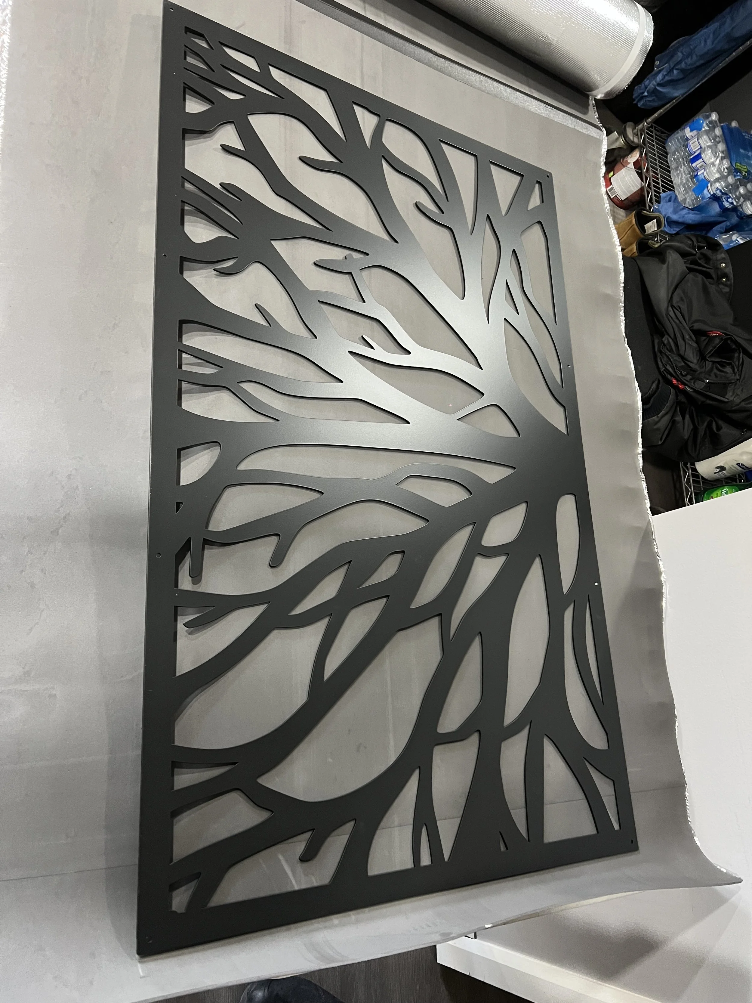 A black metal decorative panel with an intricate tree branch design, resting on a table in a workspace.