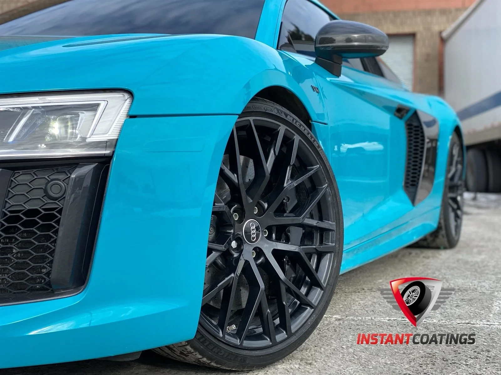 Close-up of a bright blue Audi sports car with black rims, focusing on the front left wheel and headlight.