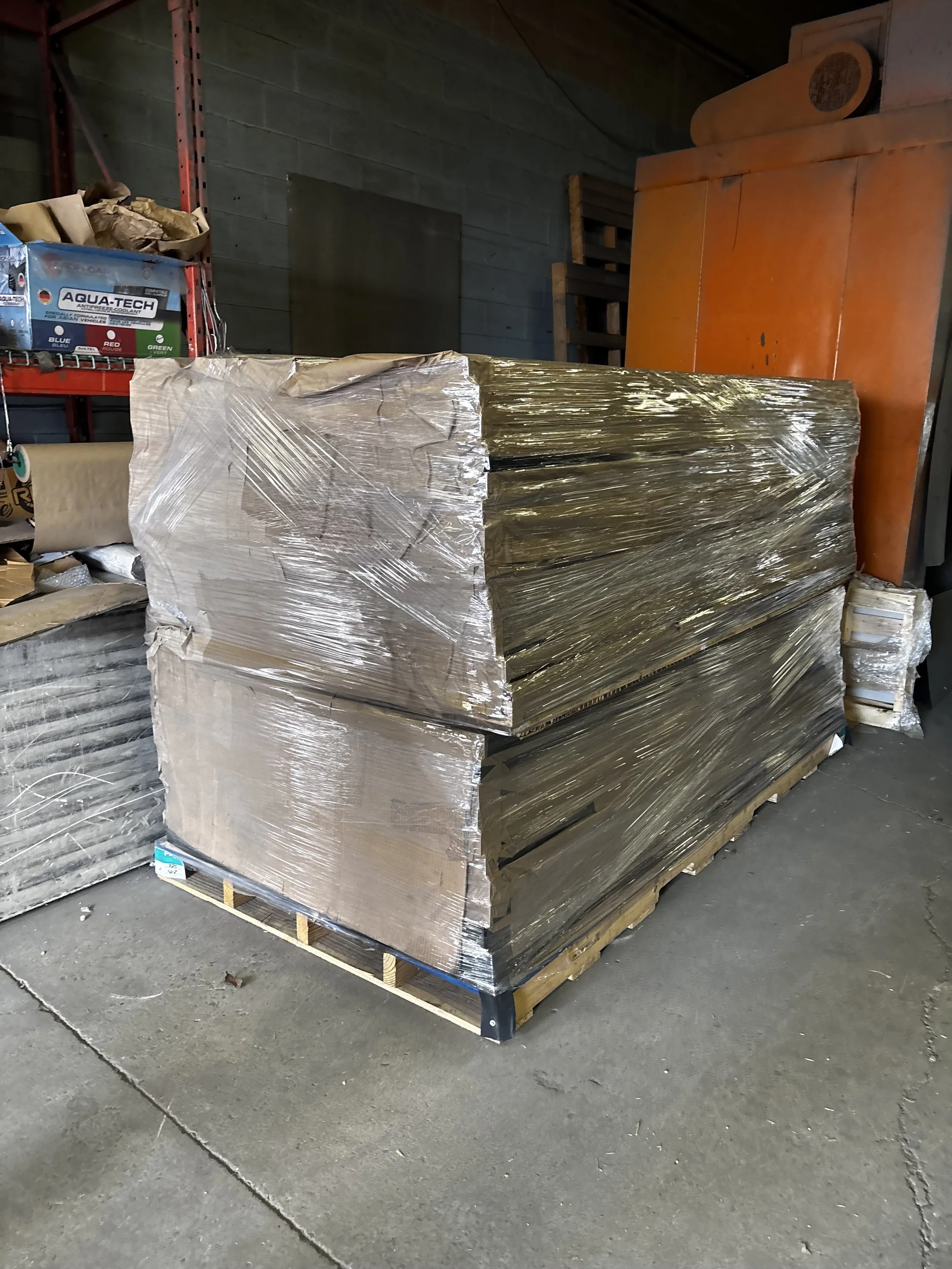 Large stack of insulated foam board panels wrapped in plastic and placed on a wooden pallet in a warehouse.