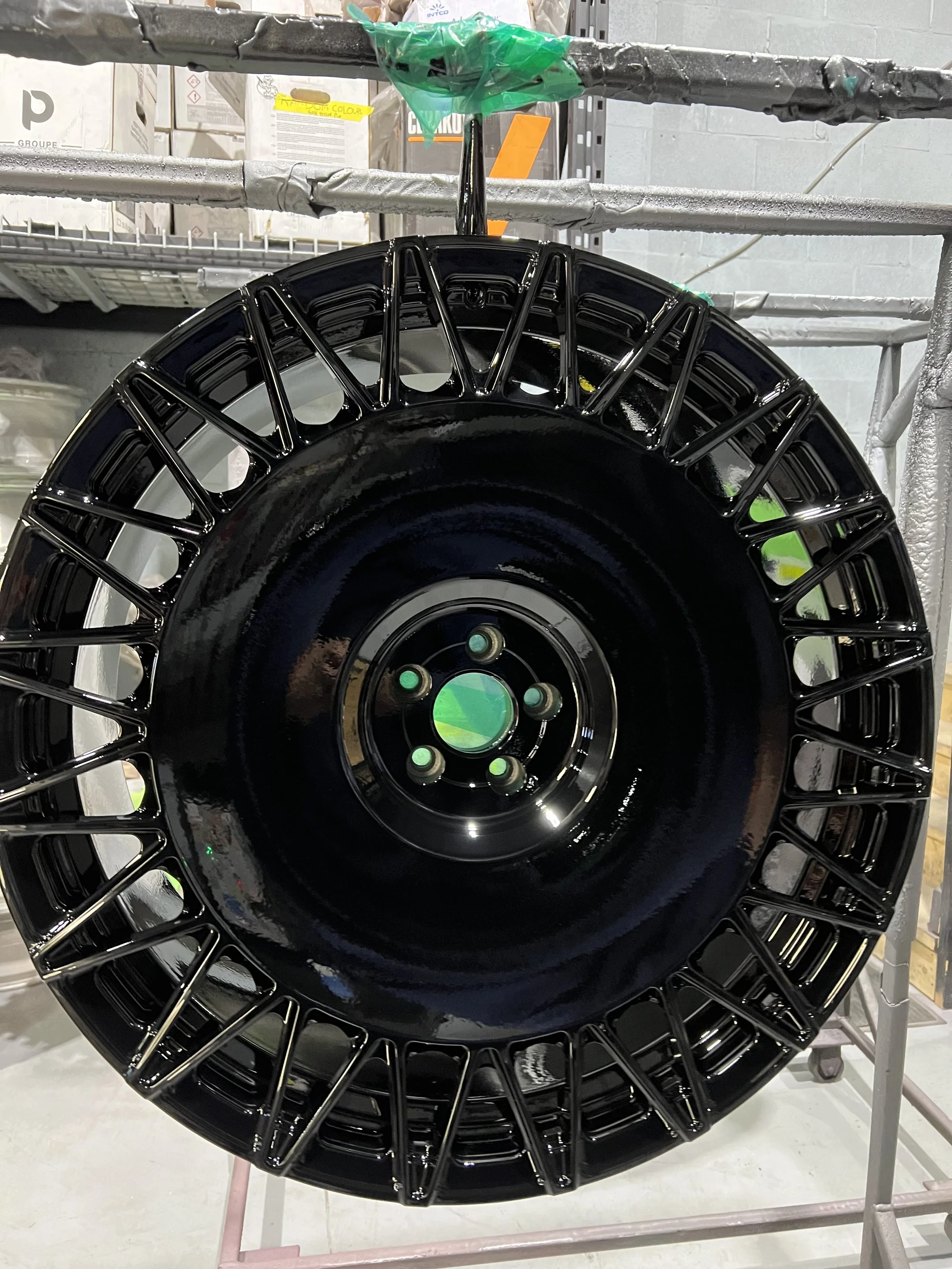 A large black wheel with a wire spoke design, likely a car wheel, is mounted on a pallet or platform in a storage or industrial setting.