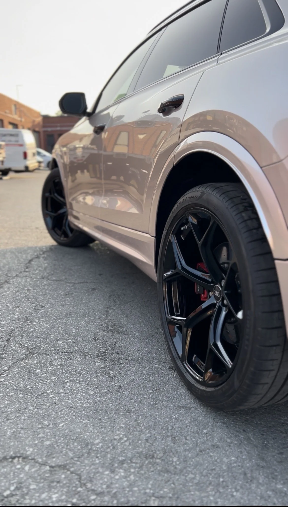 Close-up of a silver Audi SUV with black rims parked on a street, with other vehicles and buildings in the background.