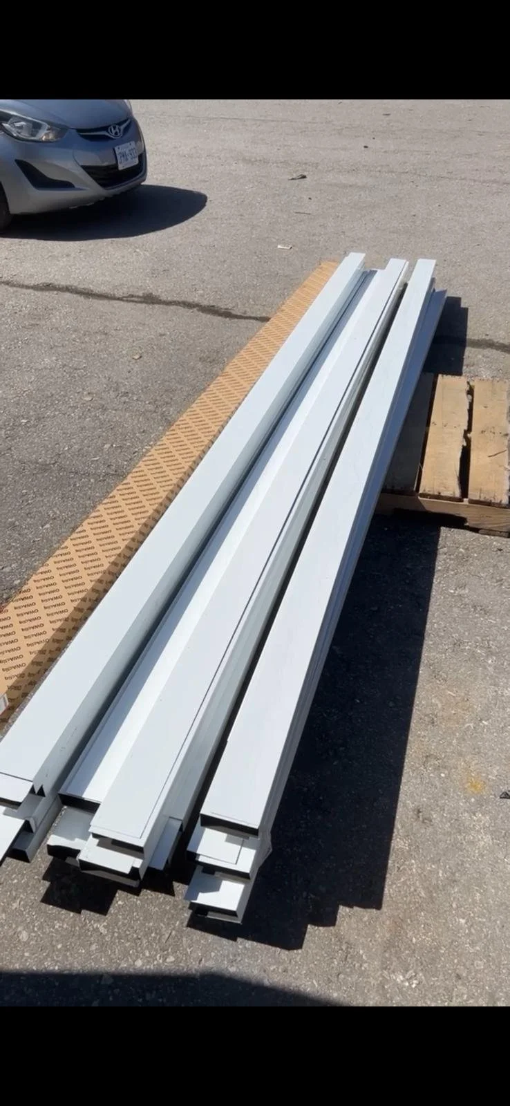 Metal and white plastic rails or tracks placed on stacked wood planks outdoors on asphalt ground.