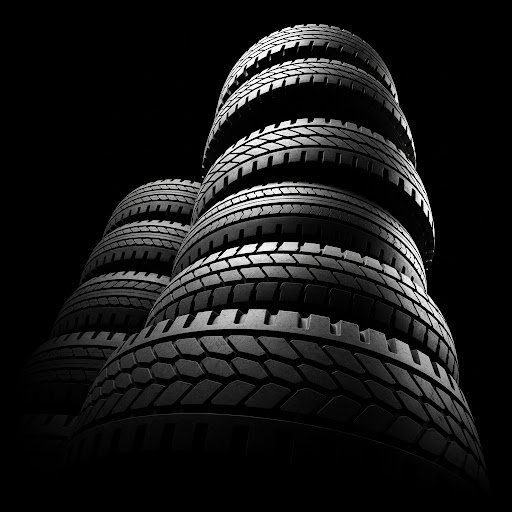 Indoor space with stacked car tires and wheels, illuminated by sunlight through windows.