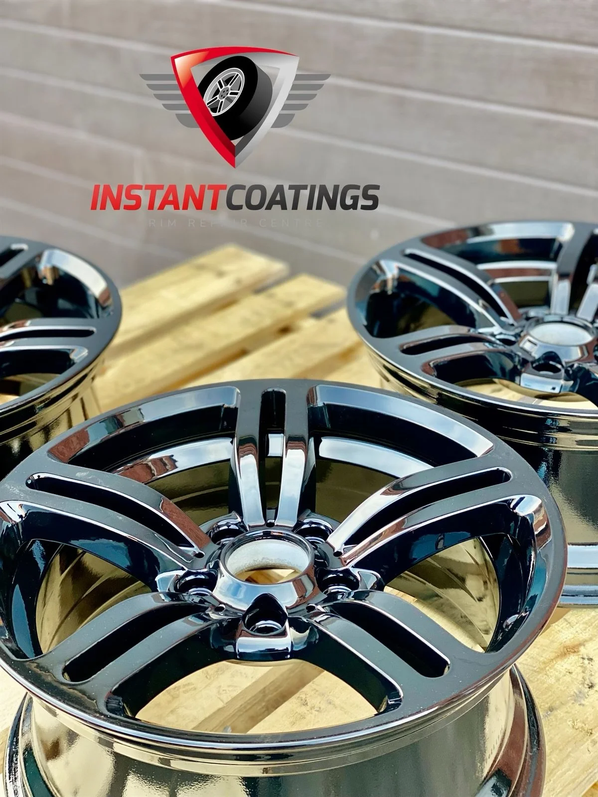 Three shiny black chrome car rims on a wooden pallet with a logo for Instant Coatings, a rim repair center, on a tiled wall background.
